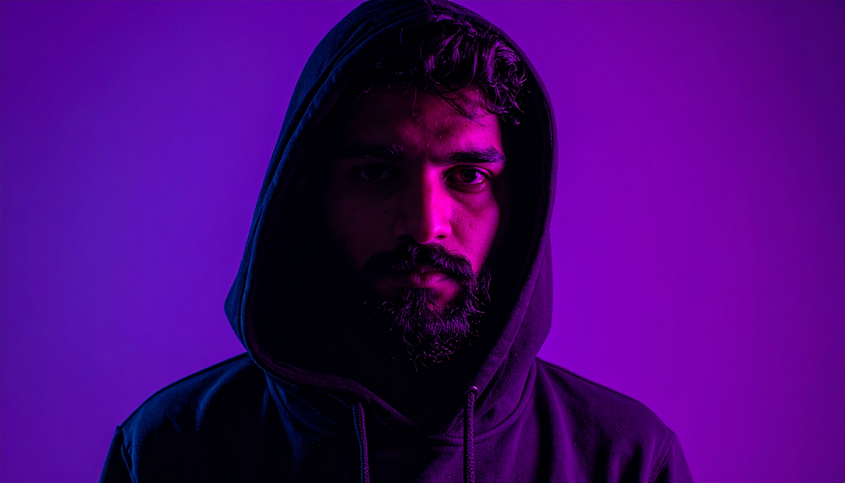 A person in a hooded sweatshirt is lit by vibrant purple and pink hues