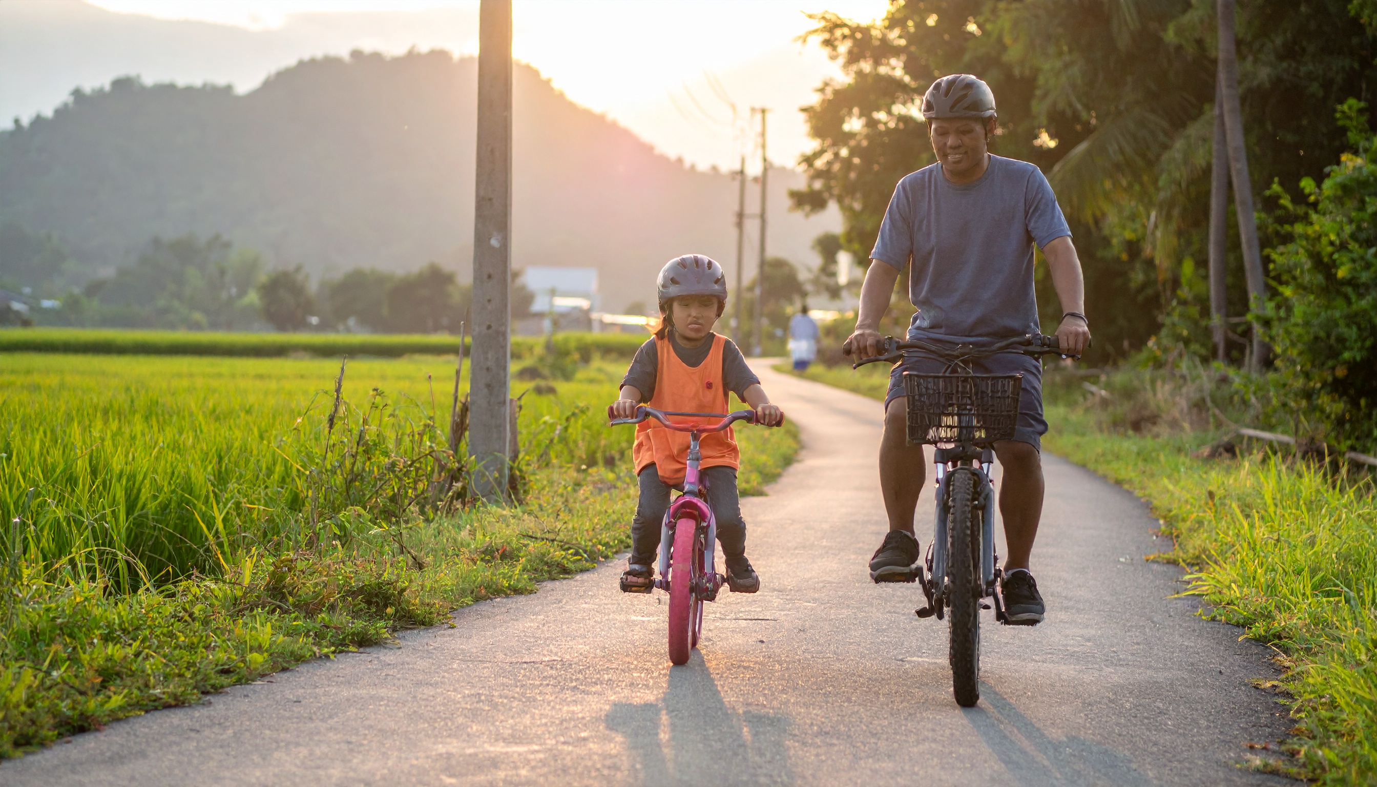 A father and child enjoy a leisurely bike ride on a rural path during sunset