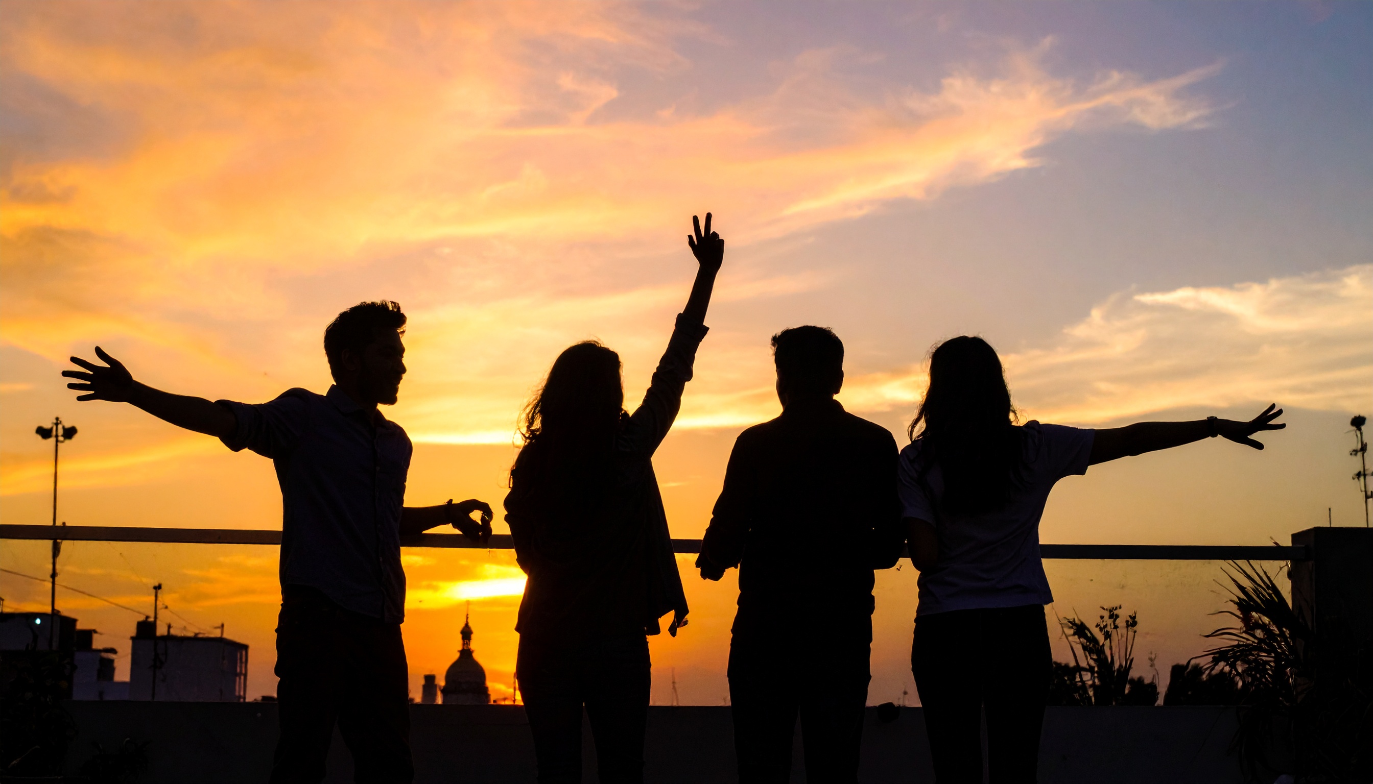 Silhouetted group of friends enjoys a vibrant sunset from a rooftop
