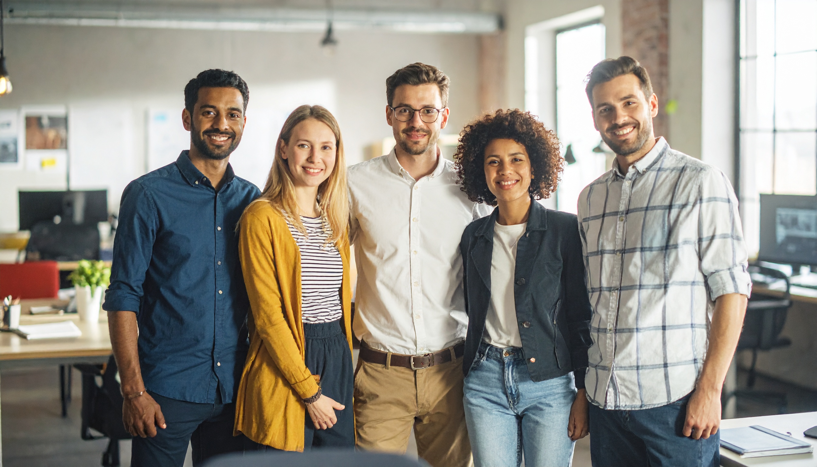 A diverse group of five professionals stands together in a modern office setting