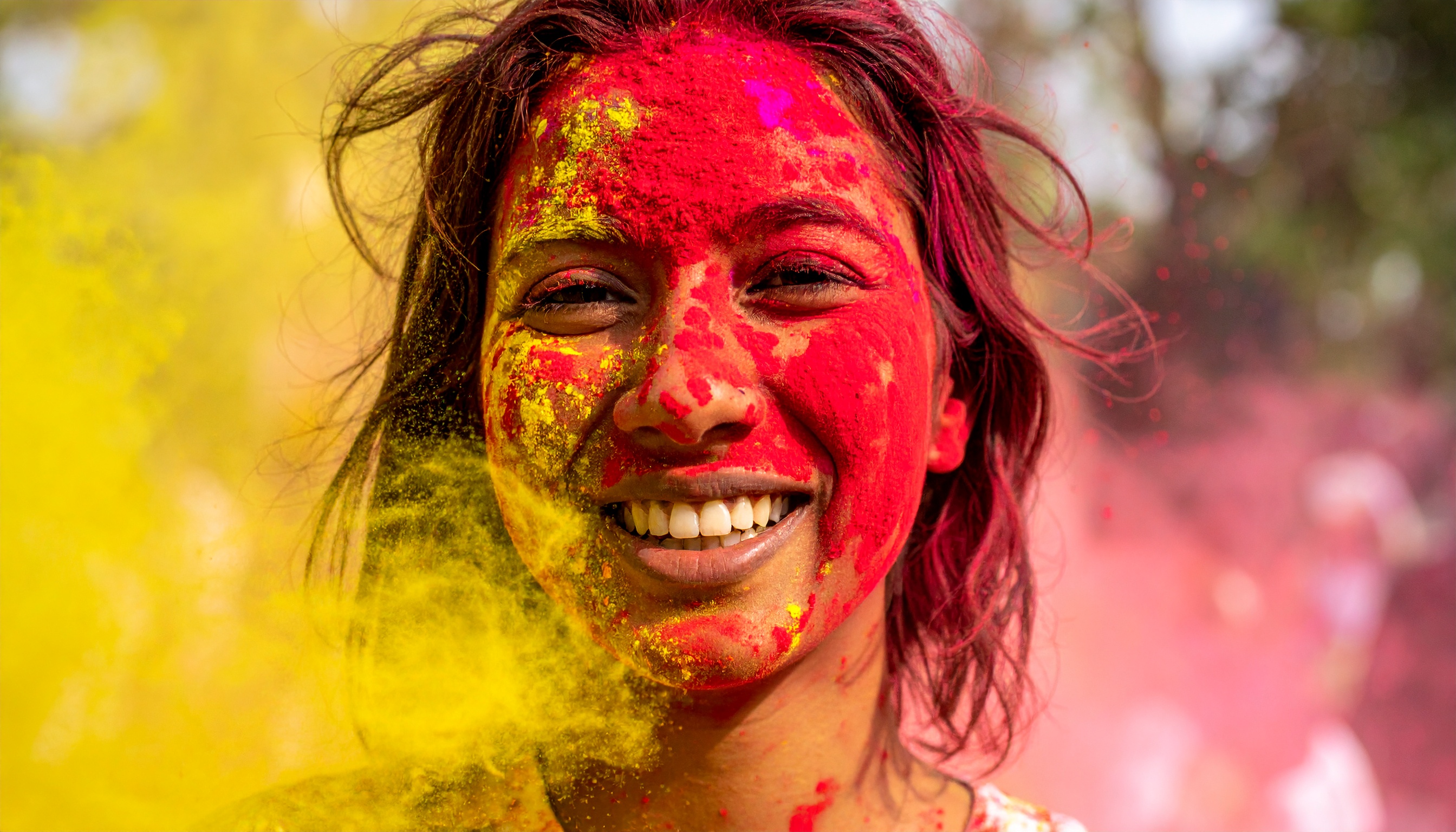 A smiling person with vibrant colors of red and yellow on their face, celebrating Holi