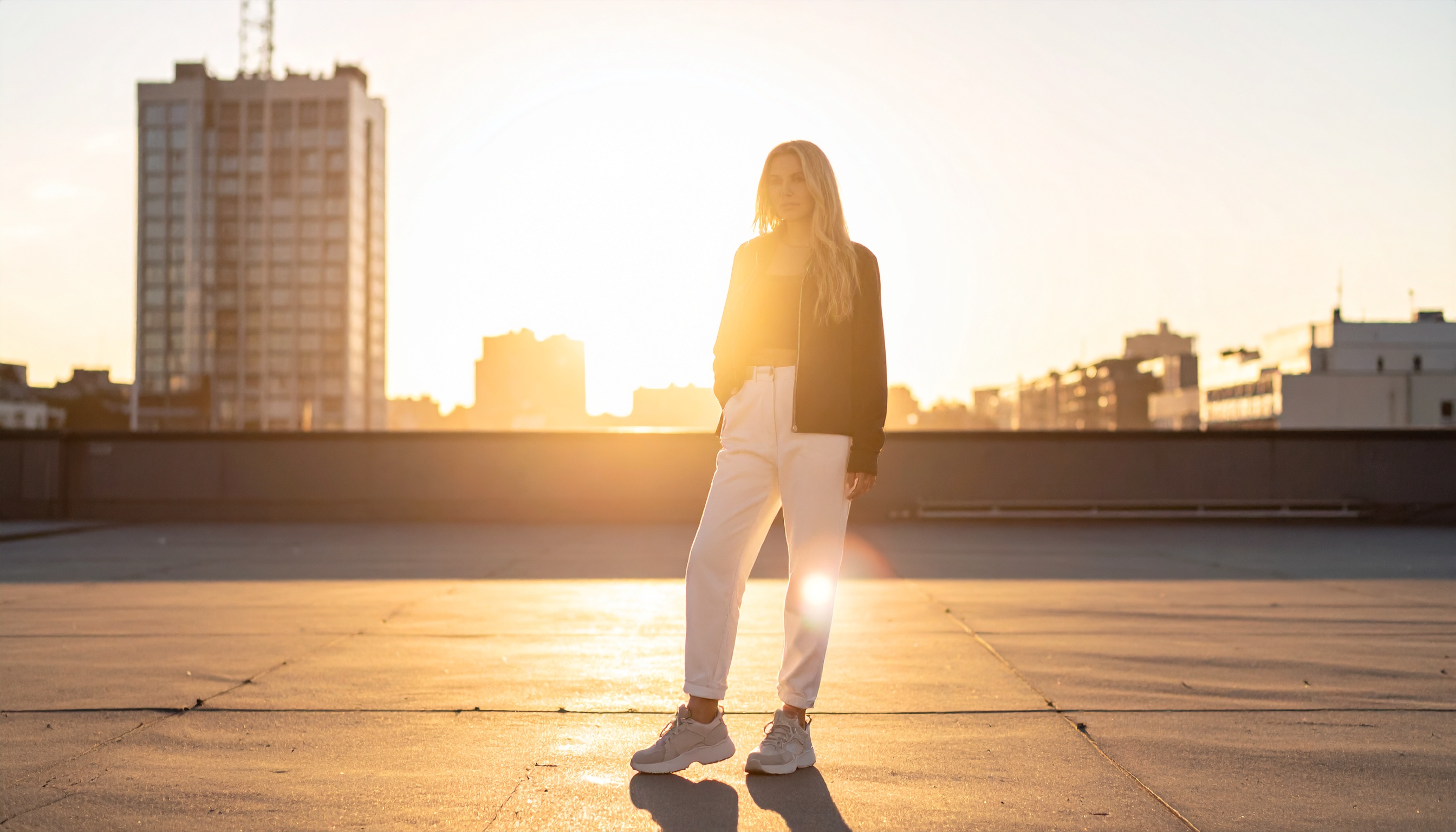 This image captures a stylish person standing on a rooftop during a stunning sunset