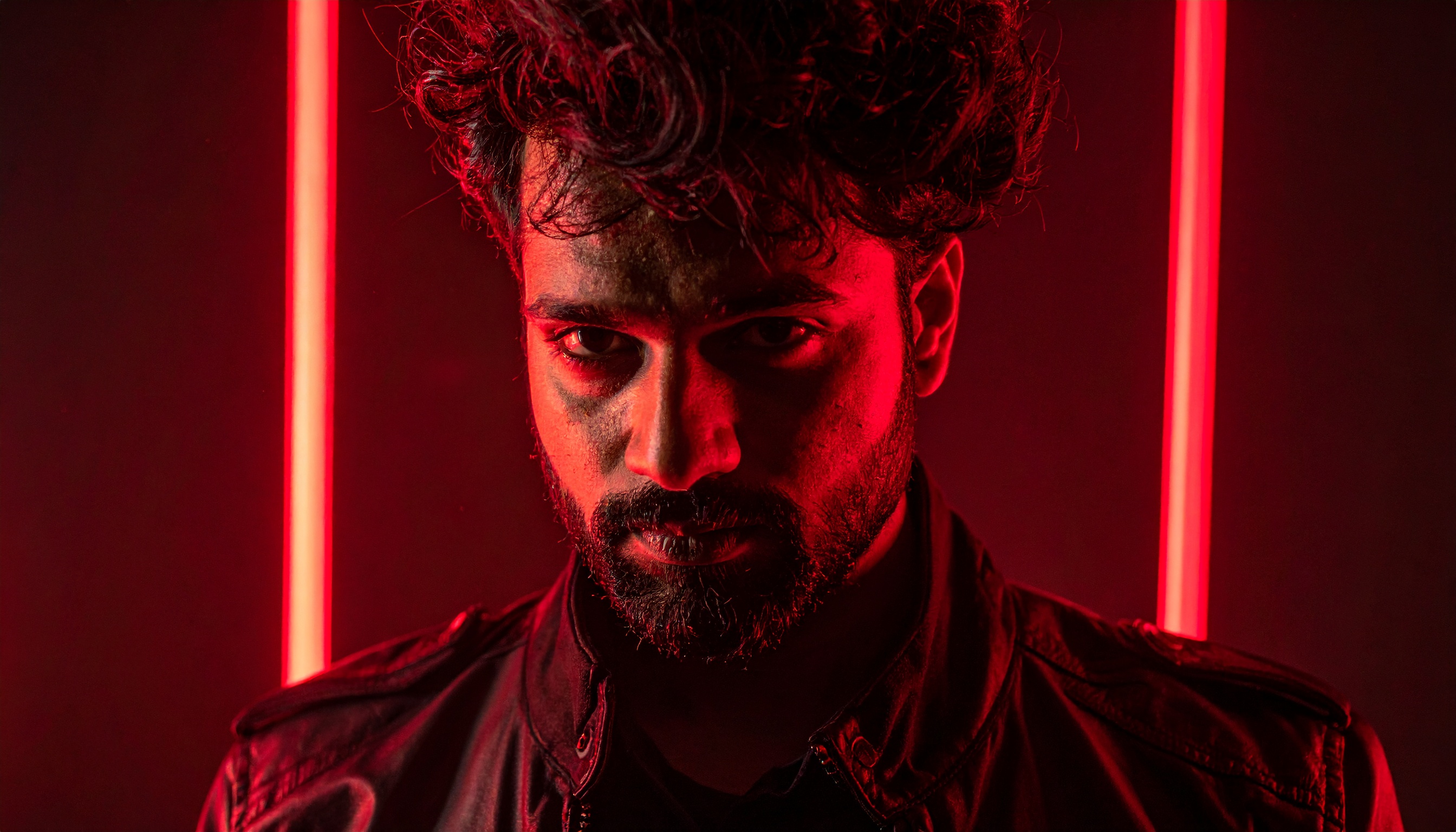 A man with intense expression stands against a background of vivid red neon lights