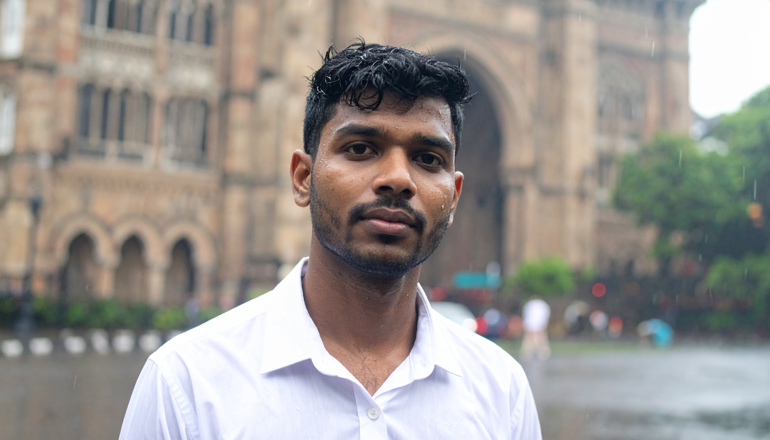 A young man stands in front of a historic building on a rainy day