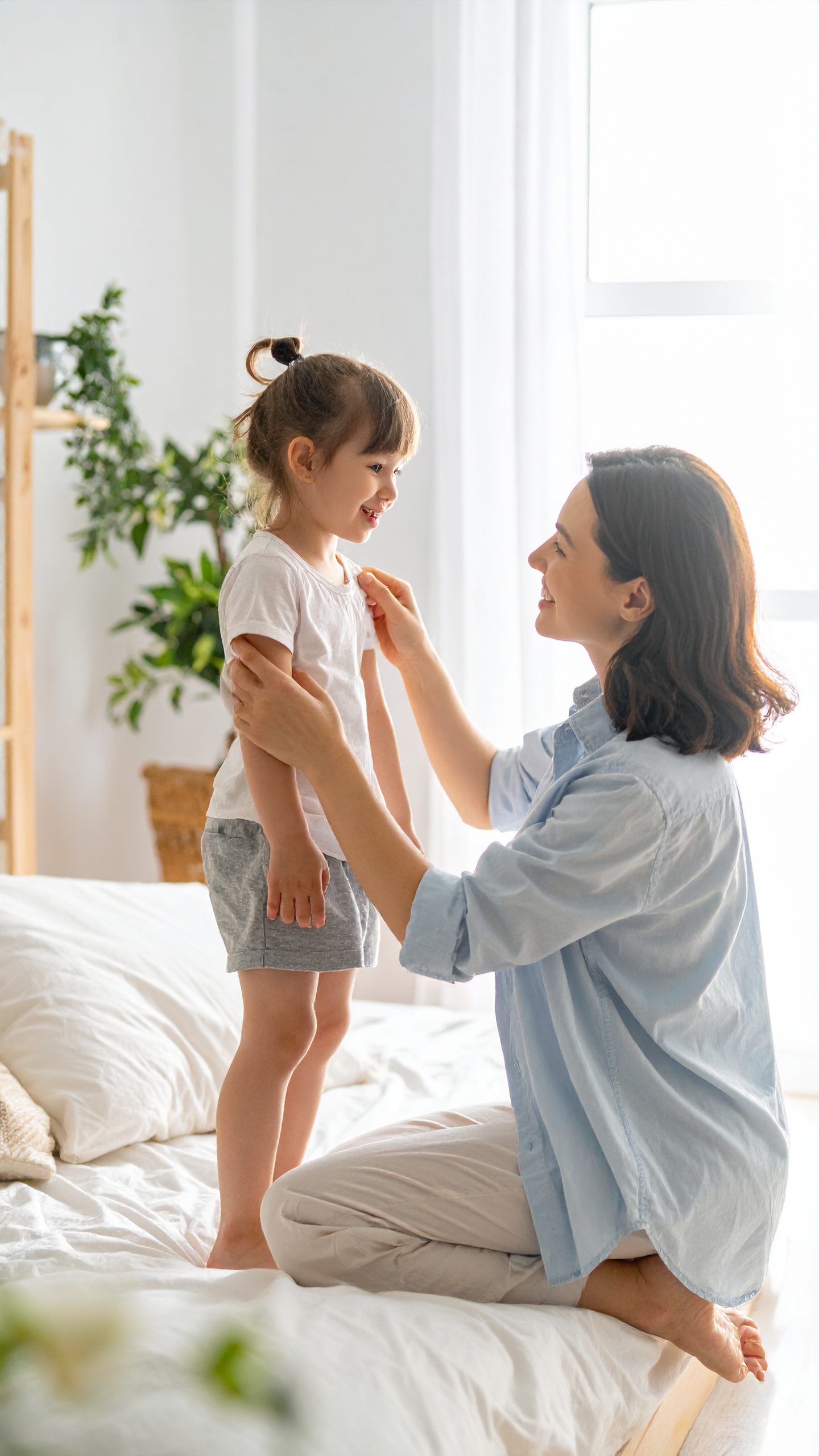 A mother is gently interacting with her young child in a cozy bedroom setting