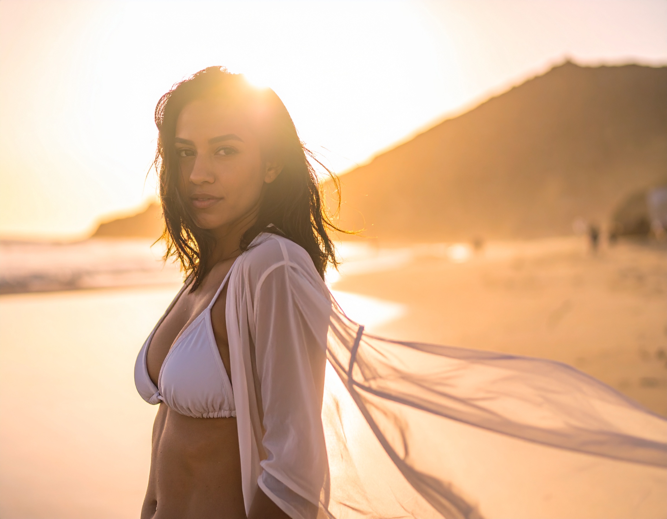 A woman in a white bikini stands on a sunlit beach