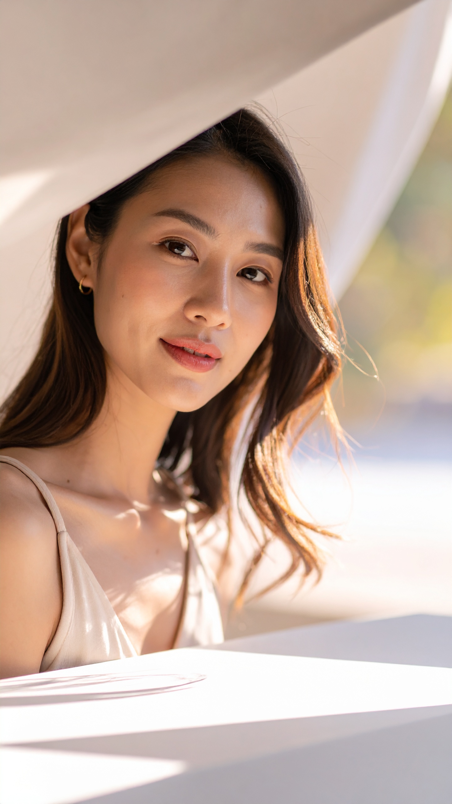 A woman with long brown hair poses in soft, natural light