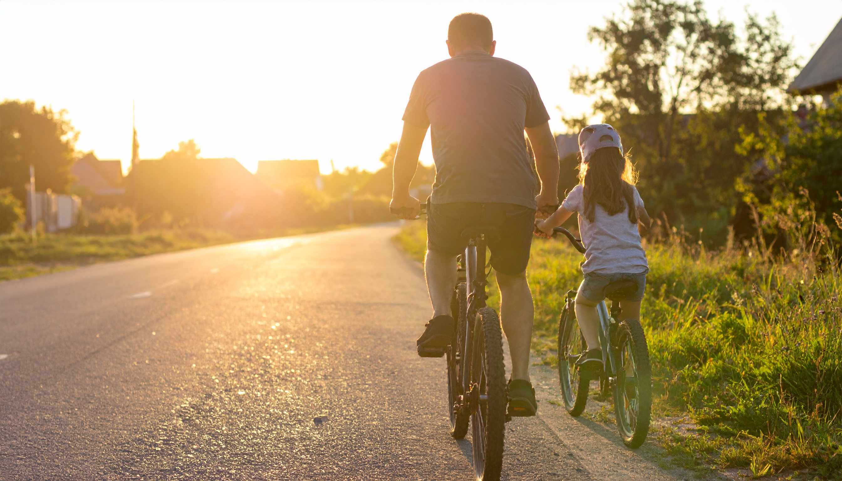 A father and daughter enjoy a bike ride on a sunny rural road at sunset
