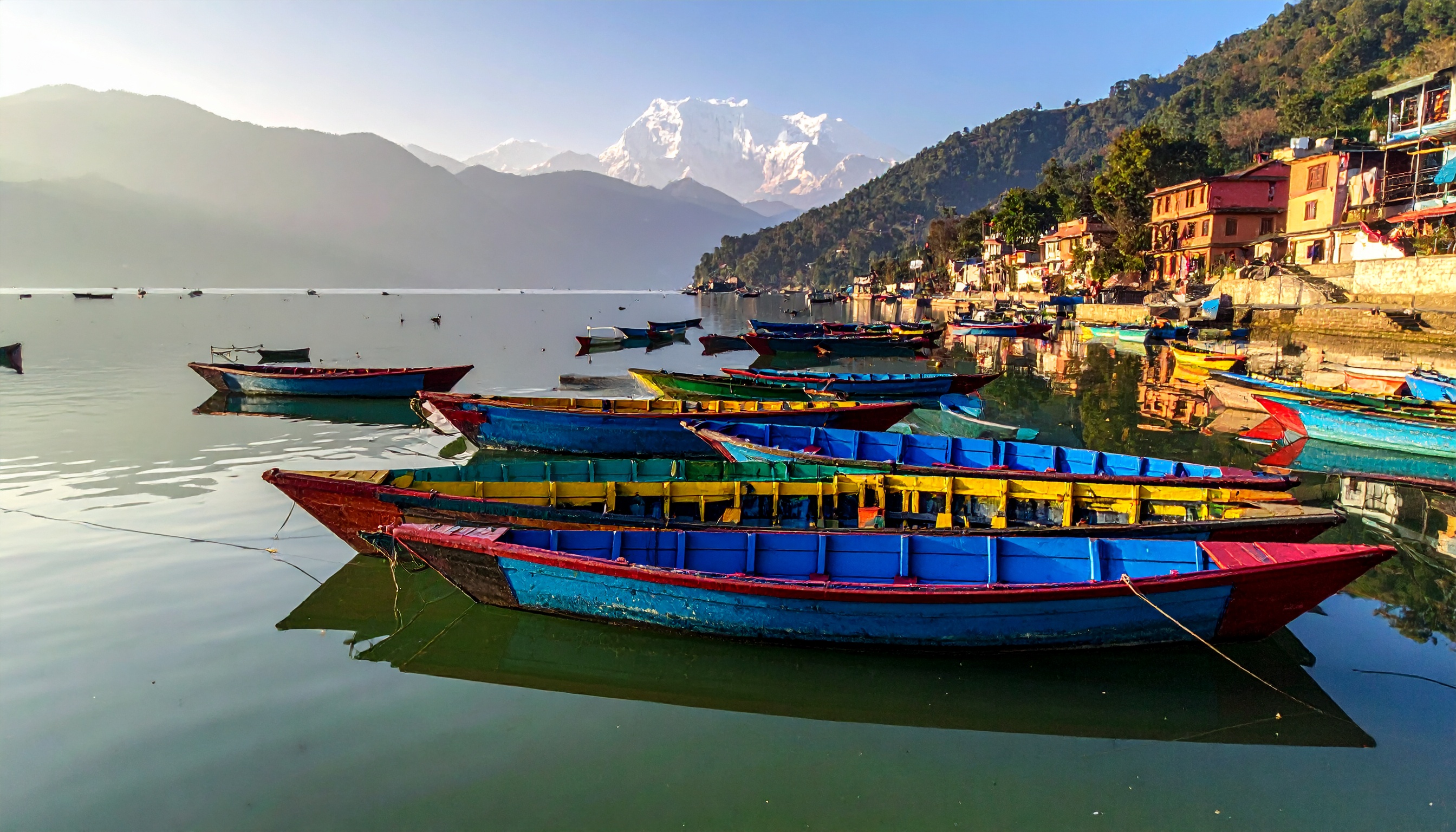 Colorful boats float on a serene lake beneath snow-capped mountains