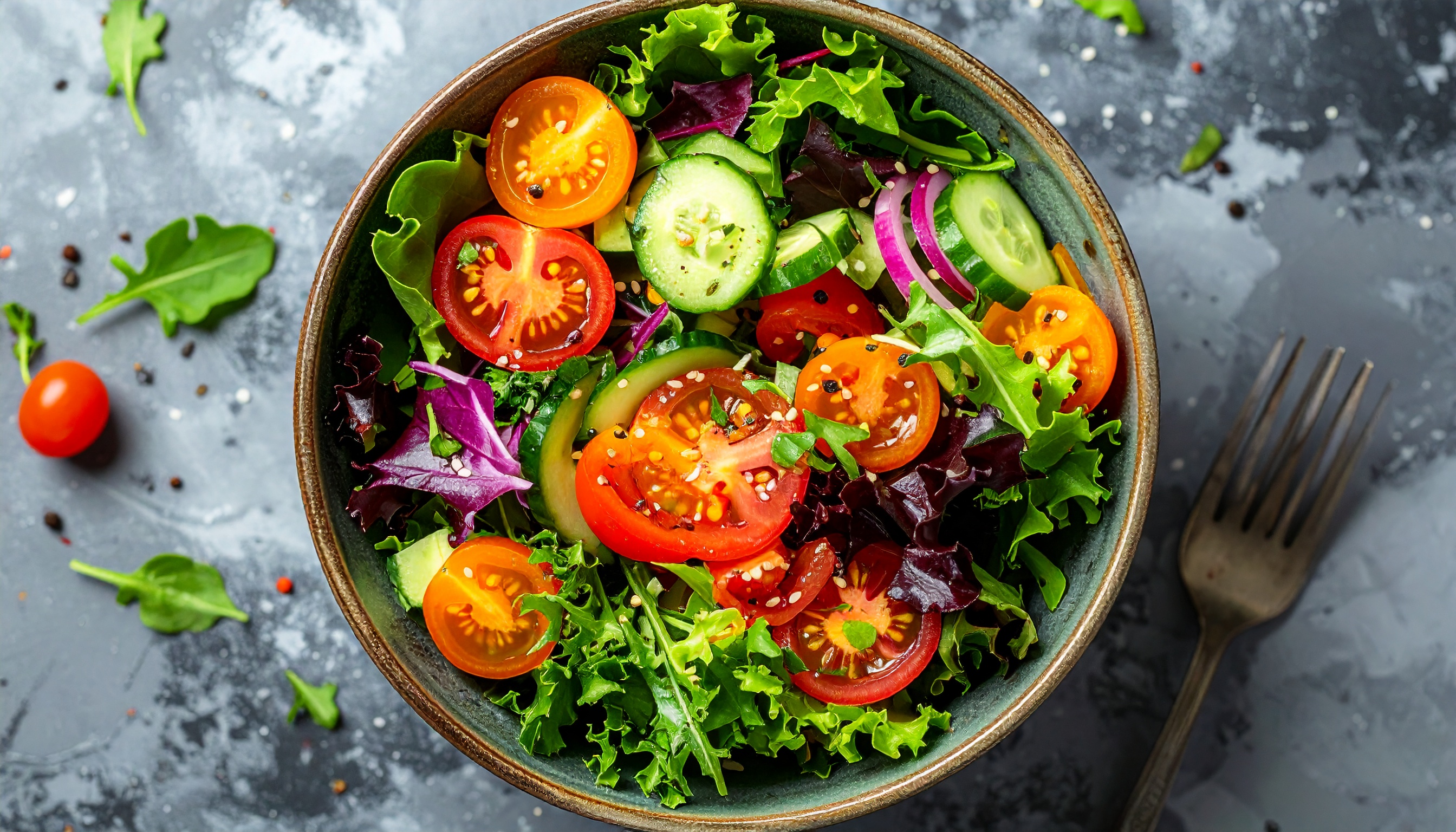 Uma vibrante salada fresca com folhas verdes, tomates cereja vermelhos e amarelos, pepinos fatiados e cebolas roxas, em uma tigela de cerâmica sobre uma superfície rústica. Ideal para receitas leves e saudáveis.