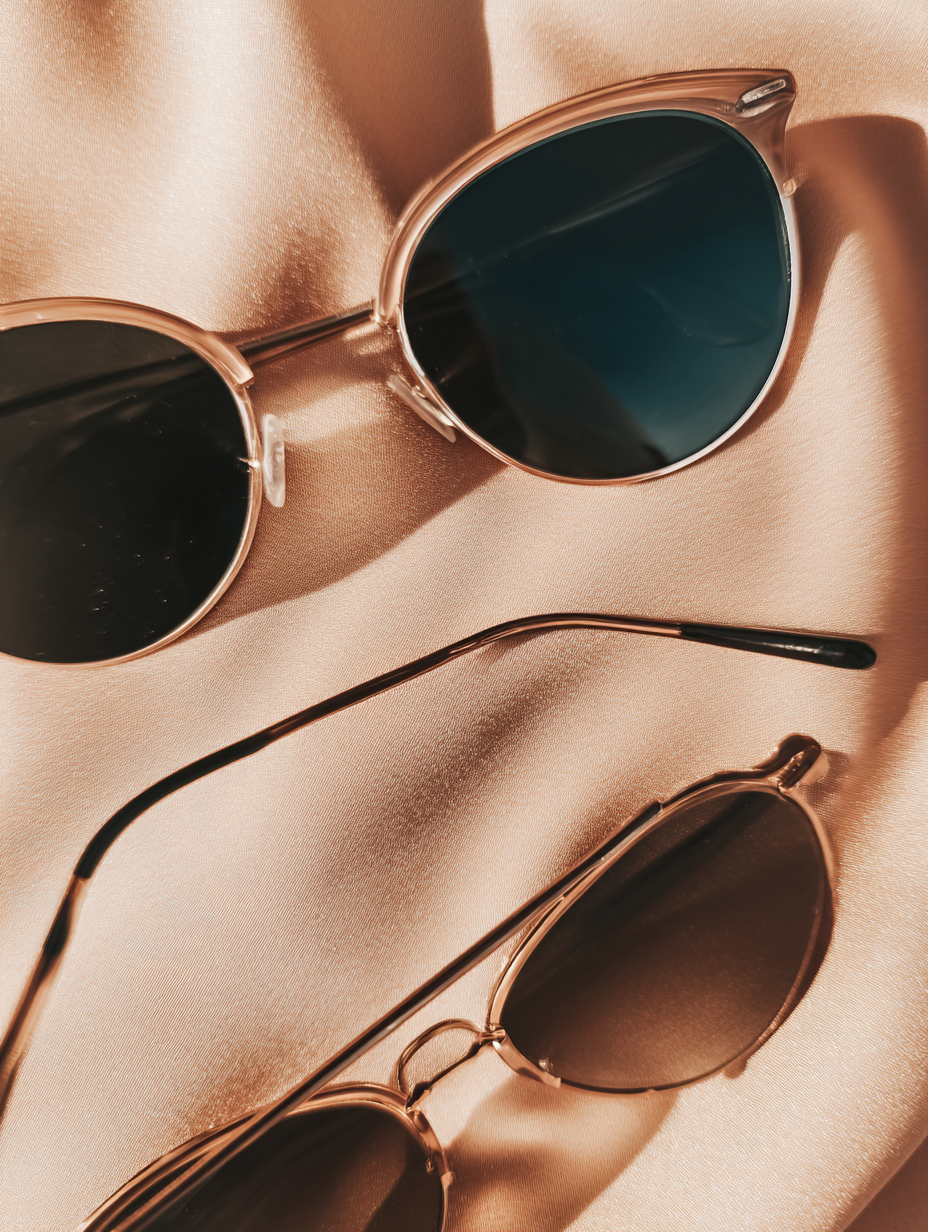 Dois óculos de sol sofisticados repousam sobre tecido de seda bege, criando uma atmosfera elegante e moderna. O reflexo suave da luz enfatiza o design clássico e o estilo chic, perfeito para moda e lifestyle.