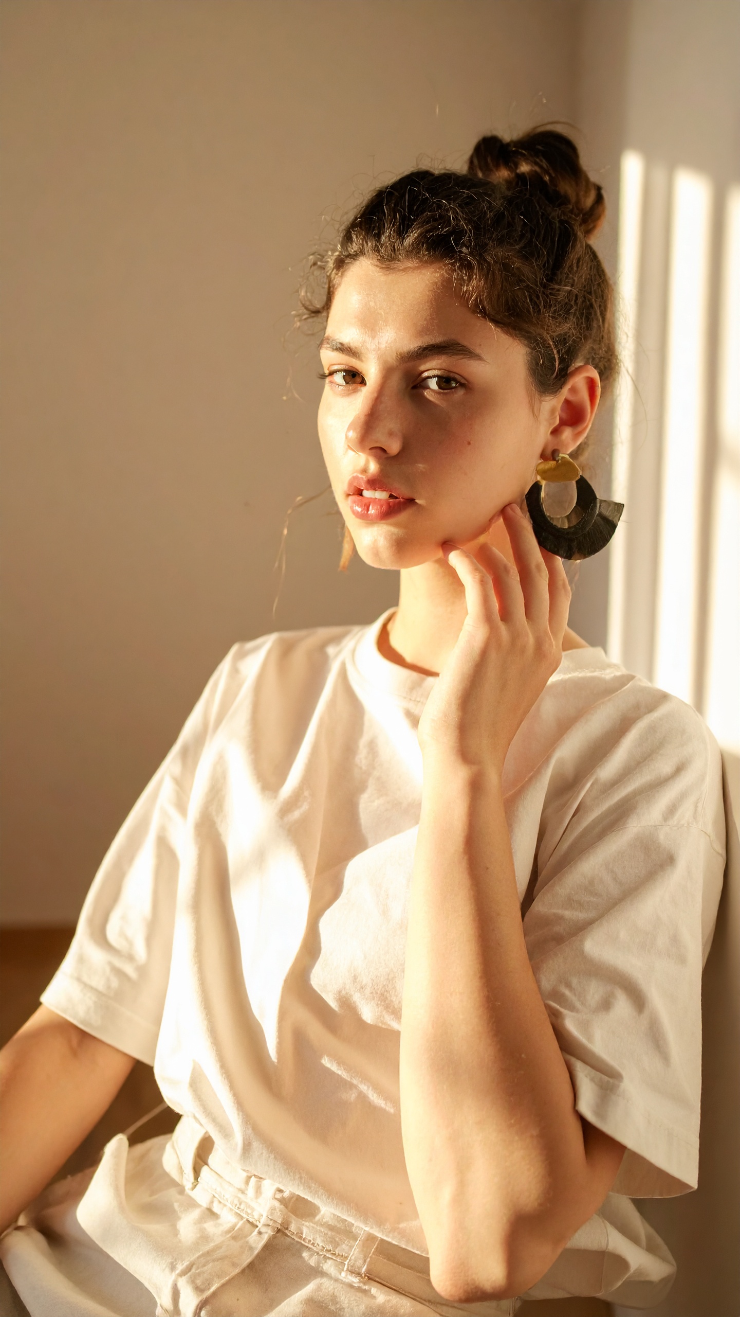 A woman in a white T-shirt basks in warm sunlight, showcasing a bold, sculptural earring