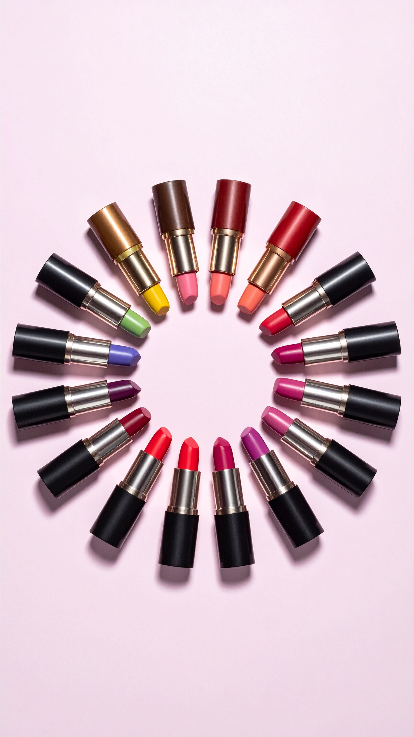 A vibrant circular arrangement of lipsticks on a soft pink background