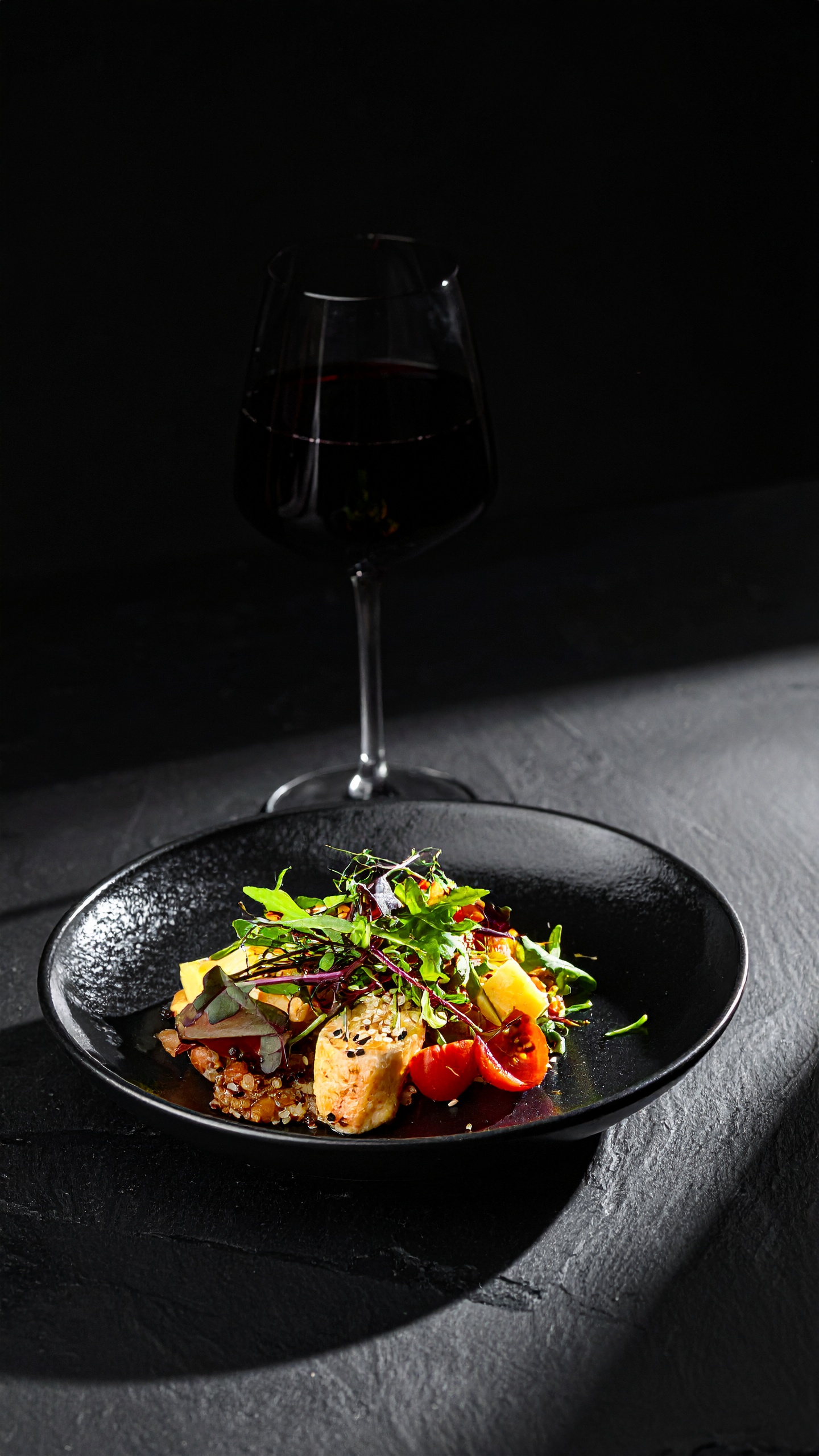 A gourmet dish is elegantly presented on a black plate, paired with a glass of red wine