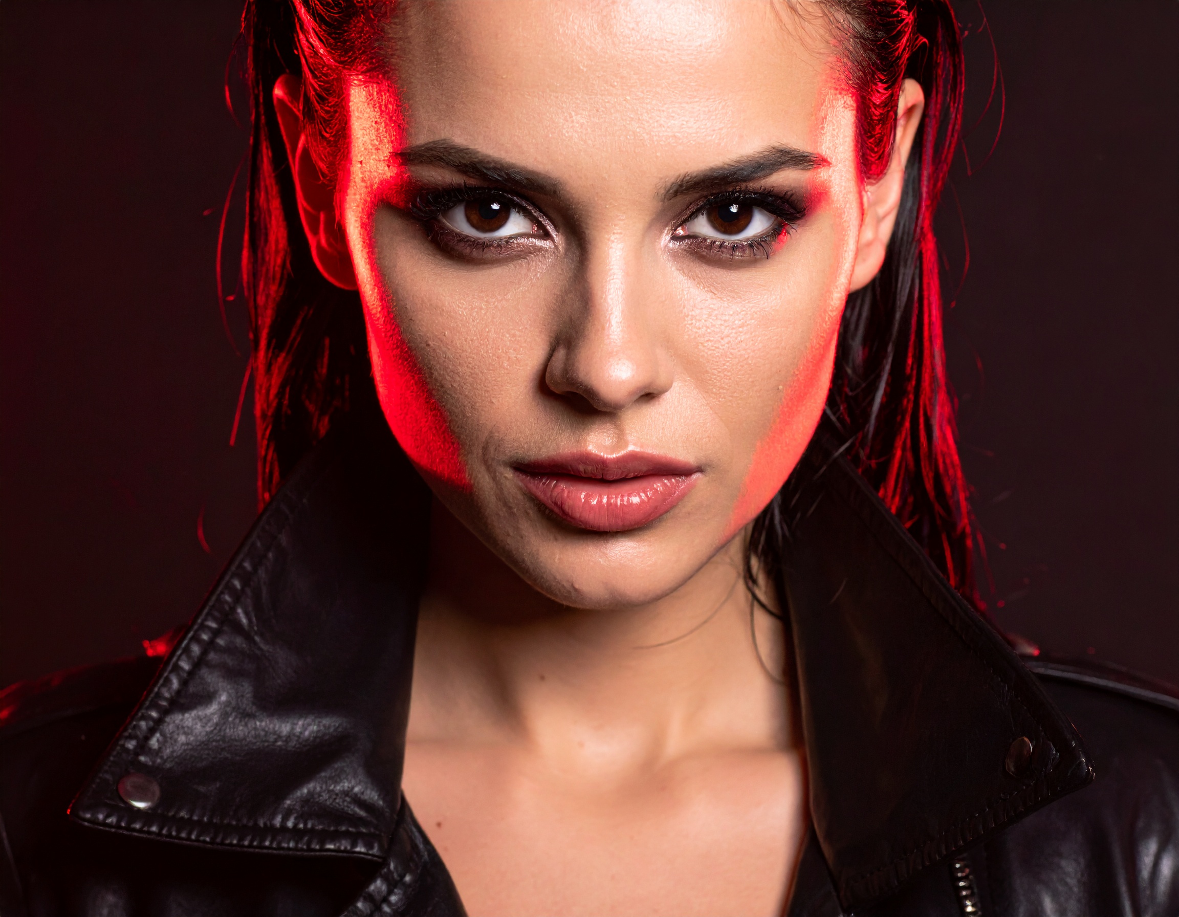 A woman in a black leather jacket is highlighted with dramatic red lighting