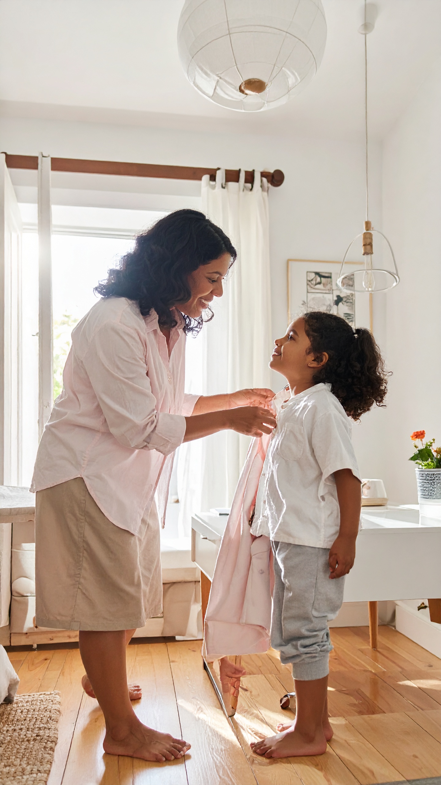 A mother helps her child get dressed in a bright, cozy room