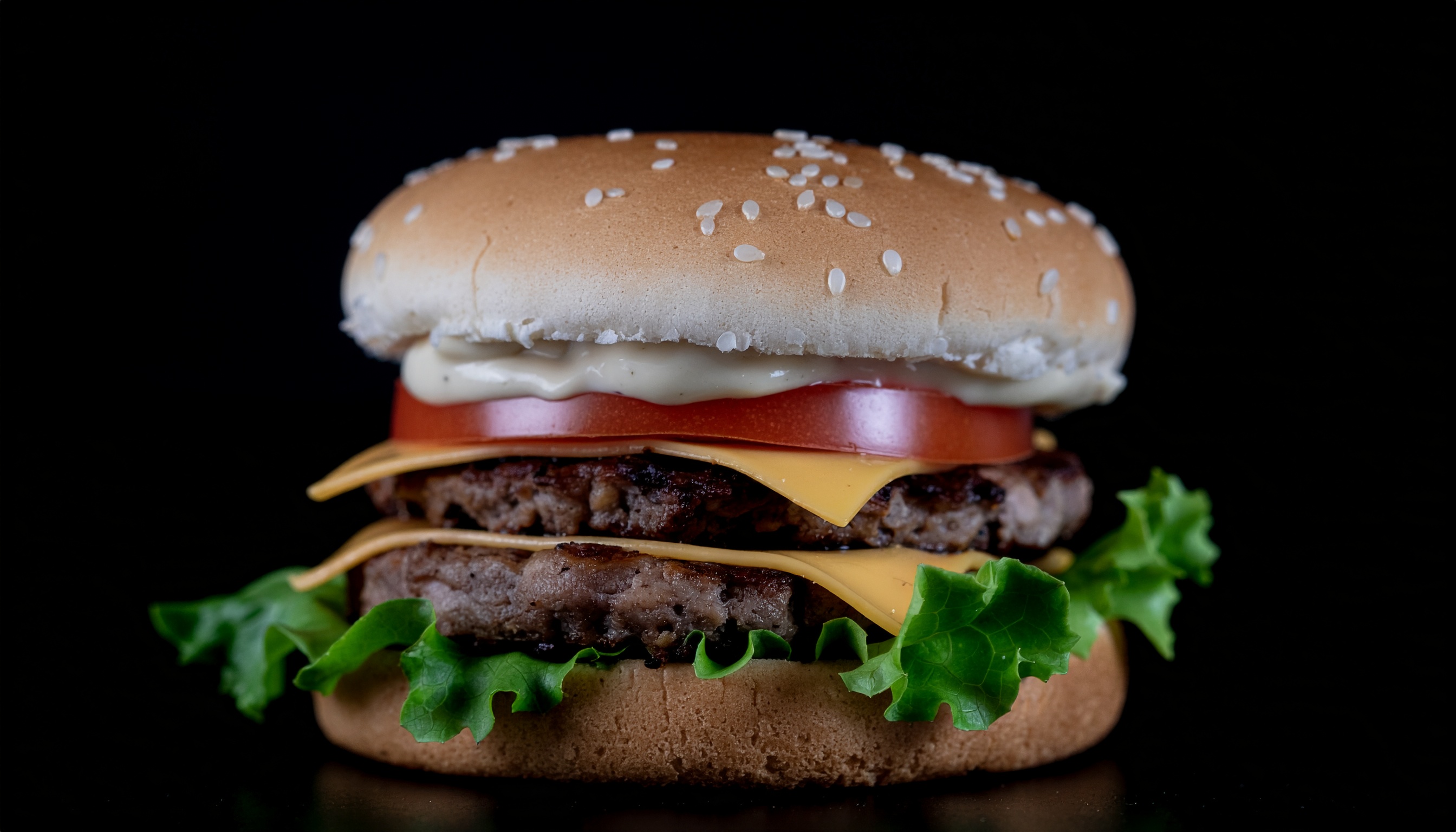 Hambúrguer suculento com pão dourado e sementes de gergelim, queijo amarelo derretido, alface verde viva e fatias de tomate, em fundo preto elegante.