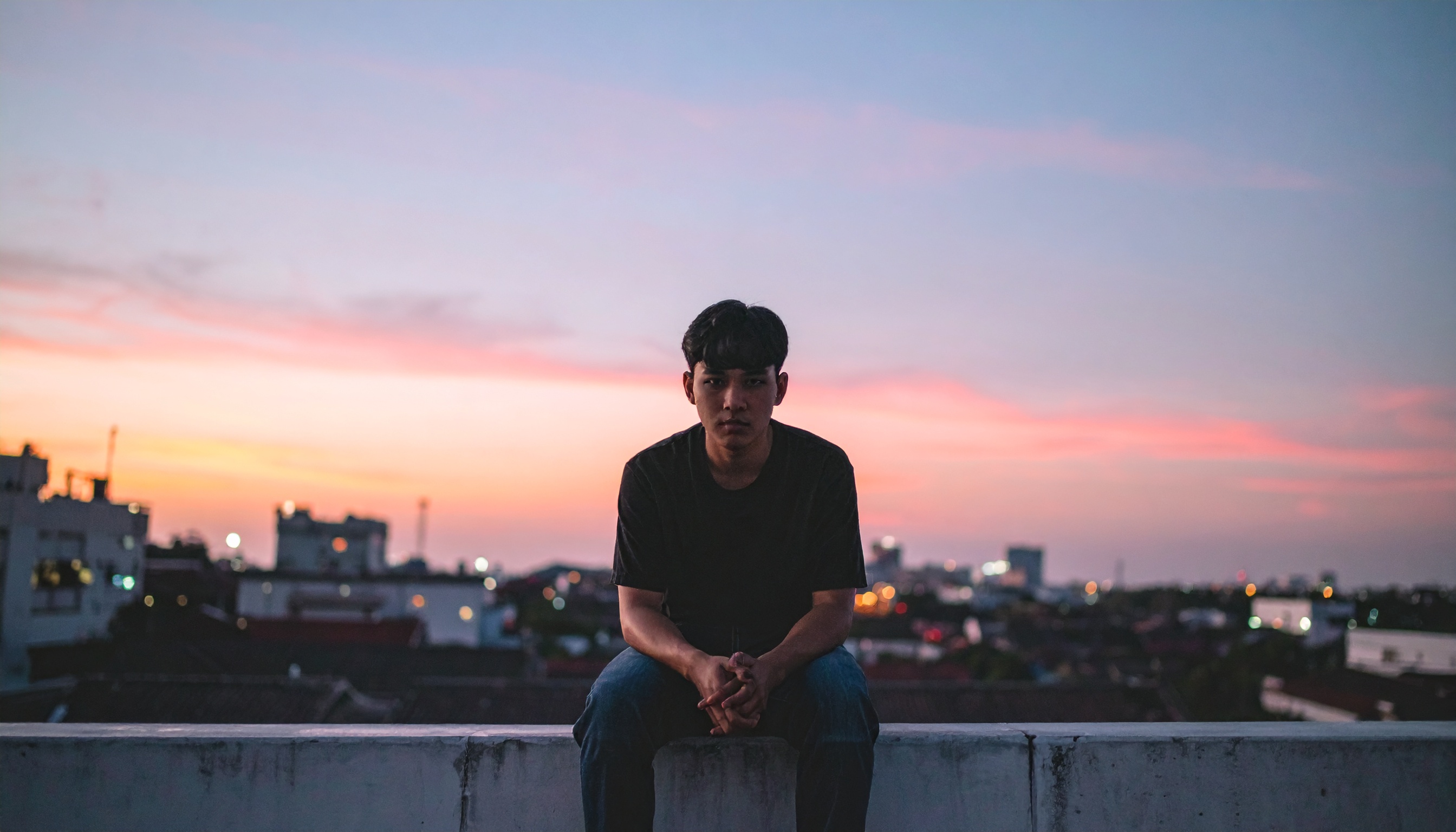 A man sits on a rooftop during a vibrant sunset, creating a contemplative scene