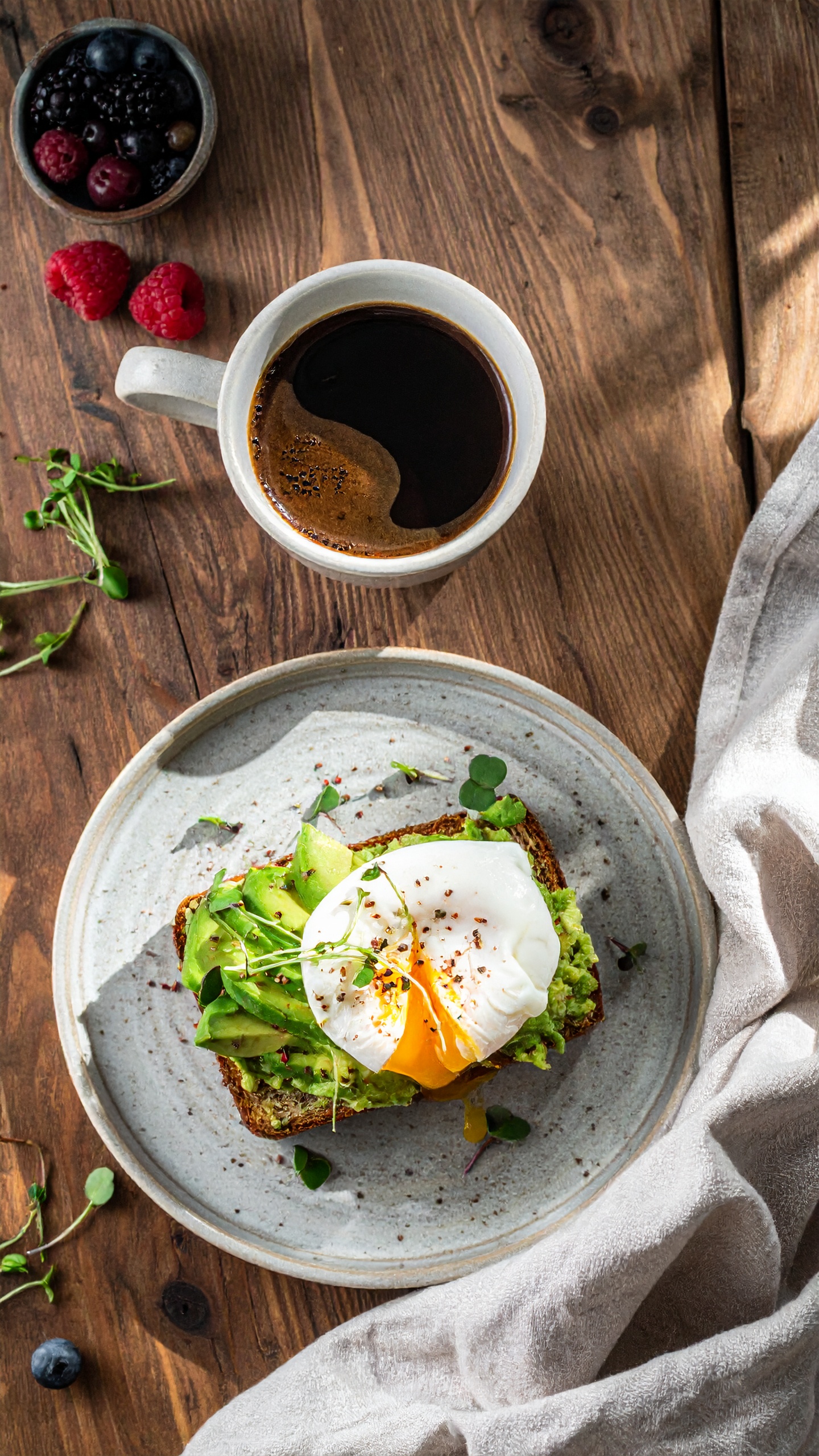 A rustic breakfast setup features avocado toast topped with a poached egg on a wooden table