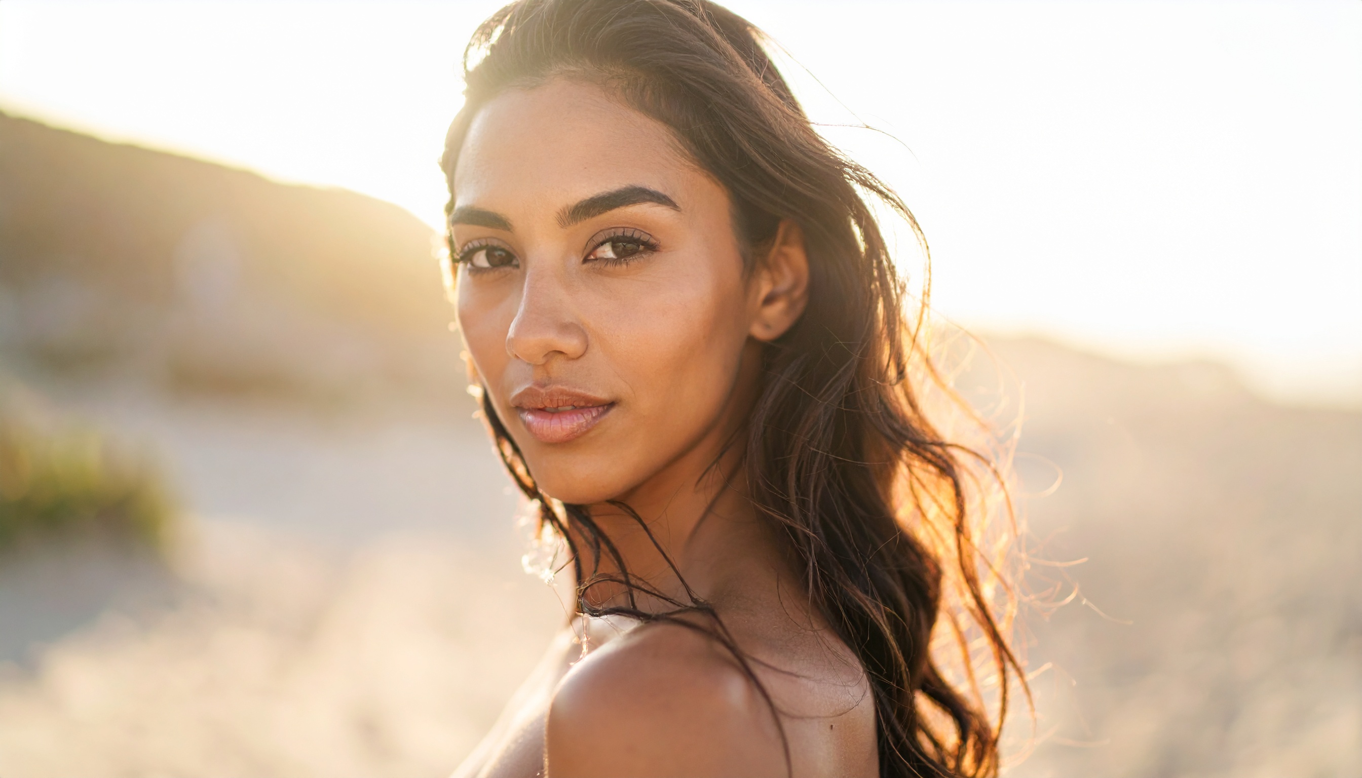 A woman with long hair gazes softly in a sunlit beach setting