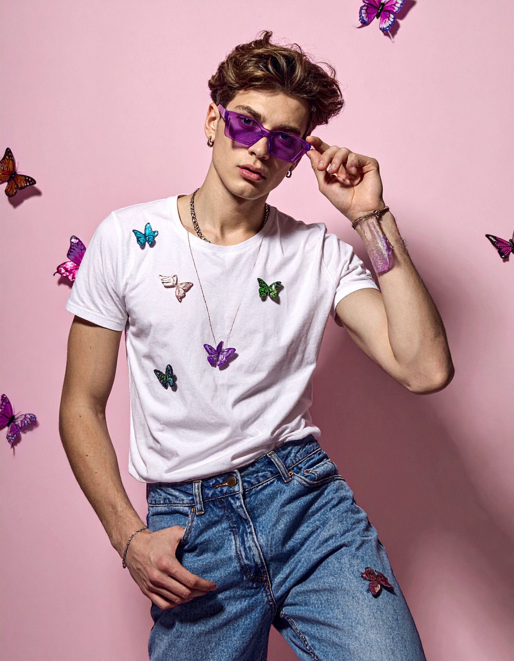 A stylish person poses confidently against a pink backdrop, wearing vibrant purple sunglasses and a