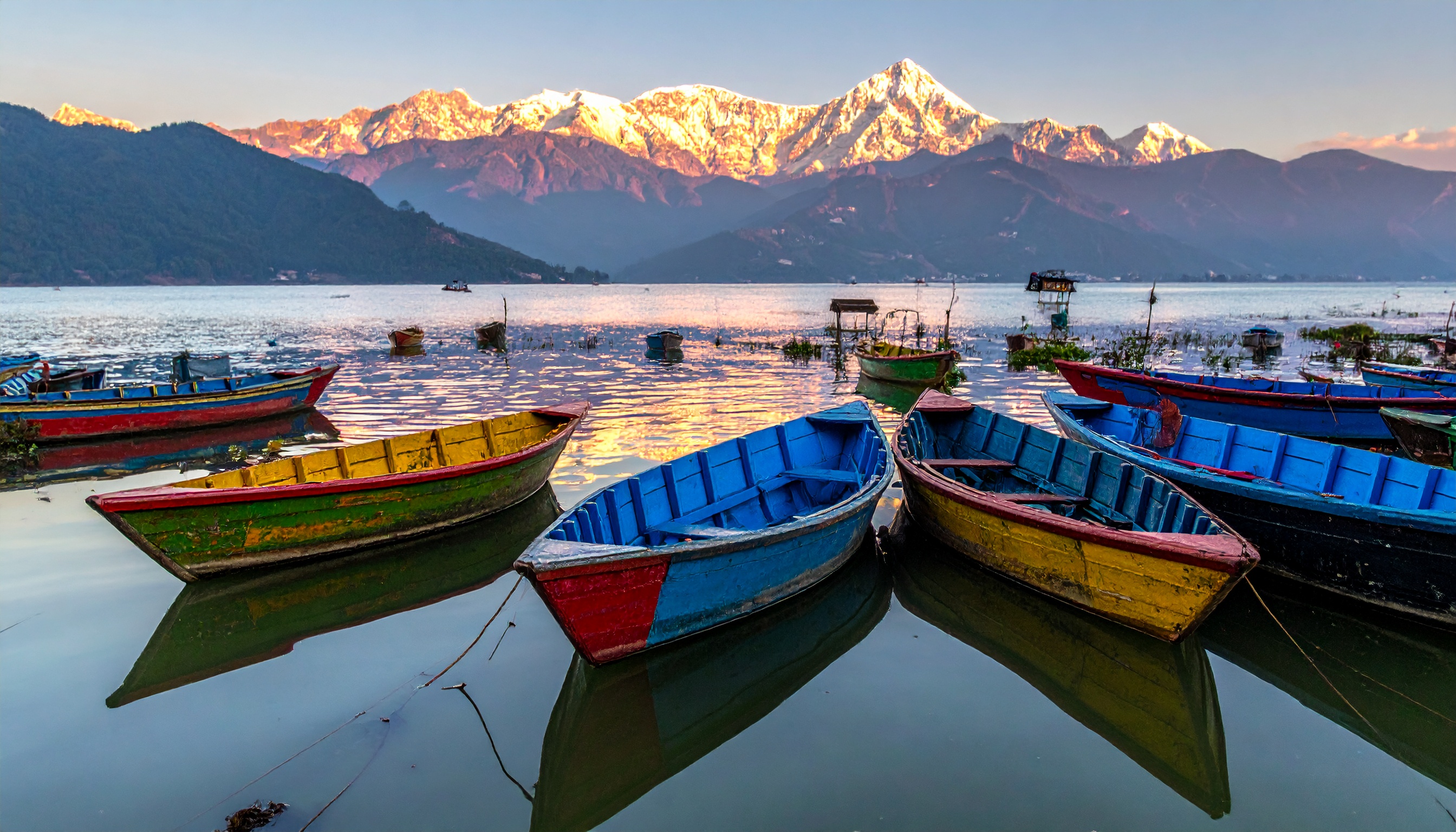 Colorful boats rest on a tranquil lake with majestic snow-capped mountains in the background