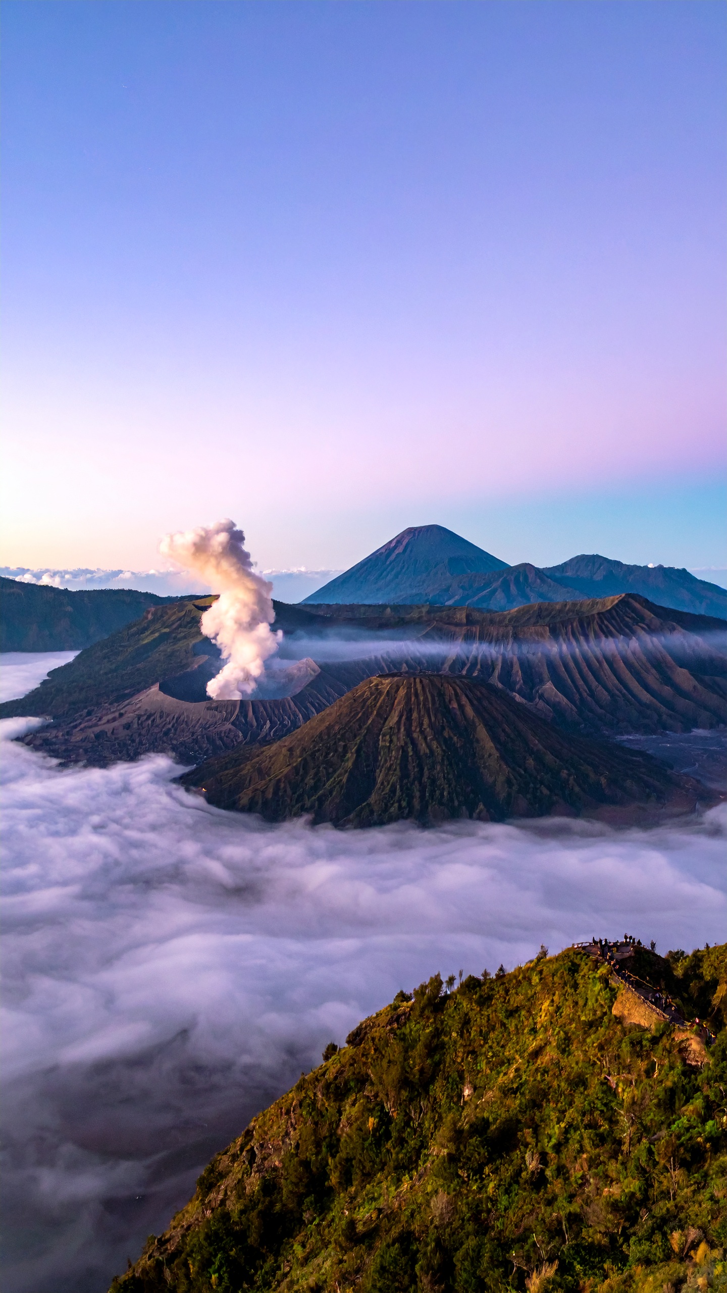 O Monte Bromo se ergue majestosamente cercado por nuvens e vegetação exuberante, criando um cenário de tirar o fôlego. Este vulcão icônico é um destino popular para aventureiros e fotógrafos em busca de capturar a beleza natural. As nuvens baixas e a luz suave do amanhecer conferem um aspecto etéreo à paisagem. Ideal para viagens de ecoturismo e exploração ao ar livre, especialmente em épocas de clima ameno. A beleza e a imponência do Bromo o tornam uma escolha perfeita para quem busca paisagens impactantes.