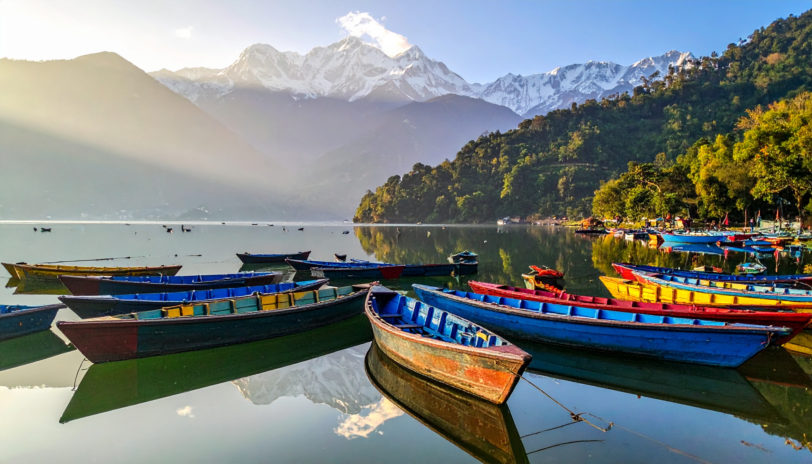 Barcos coloridos flutuam tranquilamente em um lago com montanhas ao fundo, criando uma cena serena. Esta imagem serve como um convite visual para o turismo em regiões montanhosas e lacustres. Cores vivas dos barcos contrastam com o verde das florestas e o branco das montanhas. Ideal para promover ecoturismo e destinos de aventura. Oferece uma sensação de paz e conexão com a natureza.