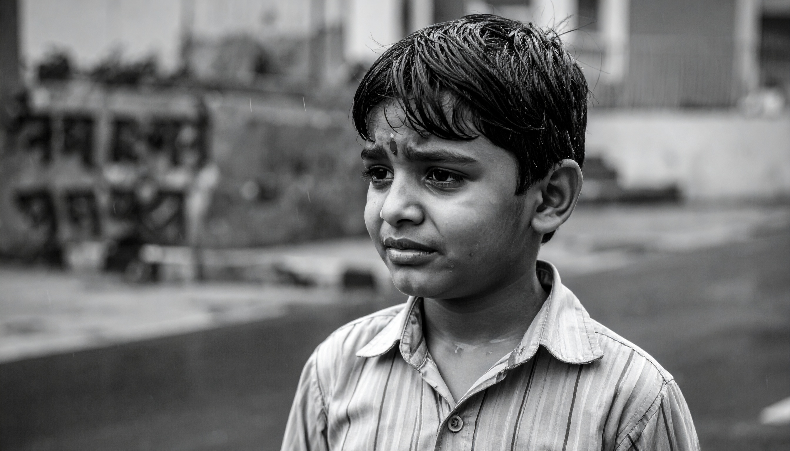 A young boy stands in the rain, his expression conveying deep emotion