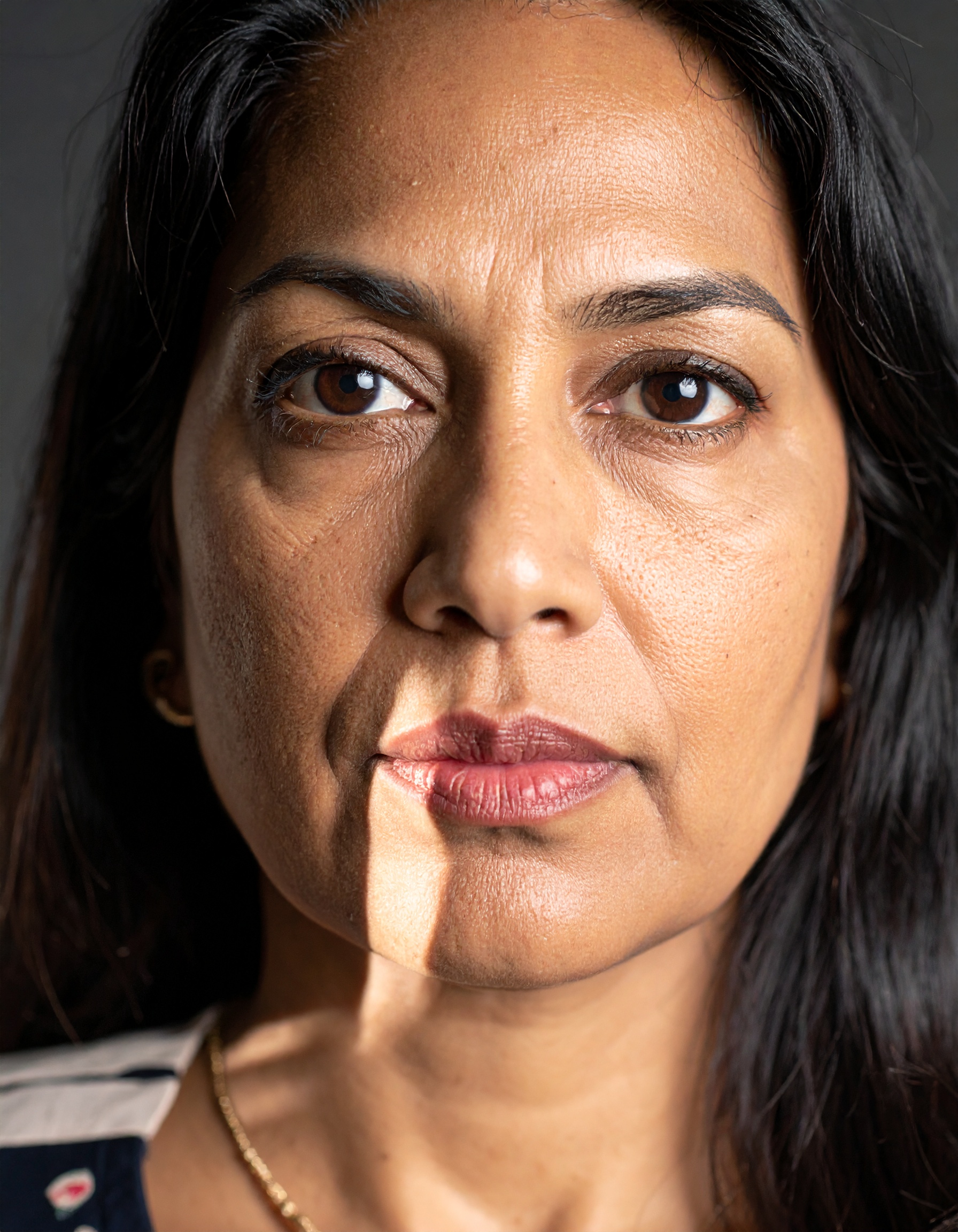 A woman's face is illuminated by a narrow beam of light, highlighting her features against