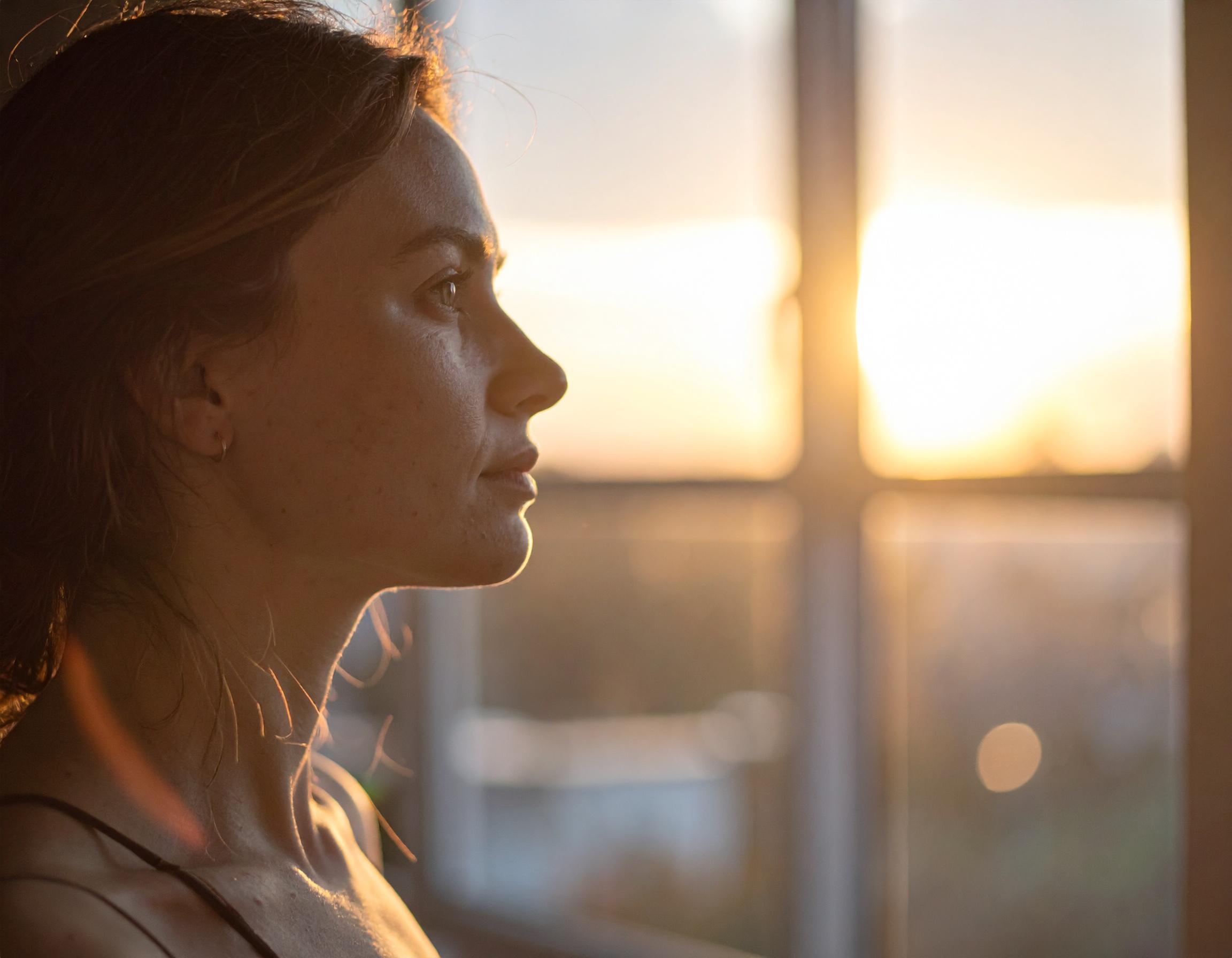 A woman is silhouetted against a warm, glowing sunset seen through a window