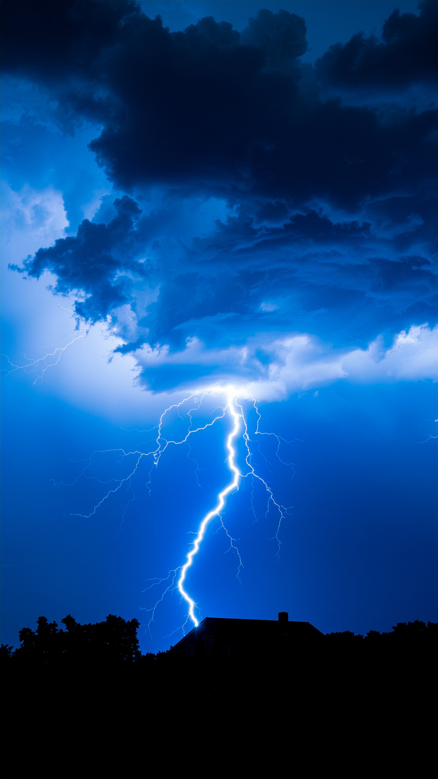 Relâmpago iluminando o céu noturno com nuvens densas e escuras. Este espetáculo natural pode ser usado em contextos educacionais ou decorativos para transmitir a força da natureza. O contraste entre o céu azul escuro e o clarão do relâmpago cria um efeito visual impressionante. Ideal para painéis educativos, ilustrações de livros ou decoração de interiores com temática natural. A imagem transmite uma sensação de poder e grandeza da natureza.