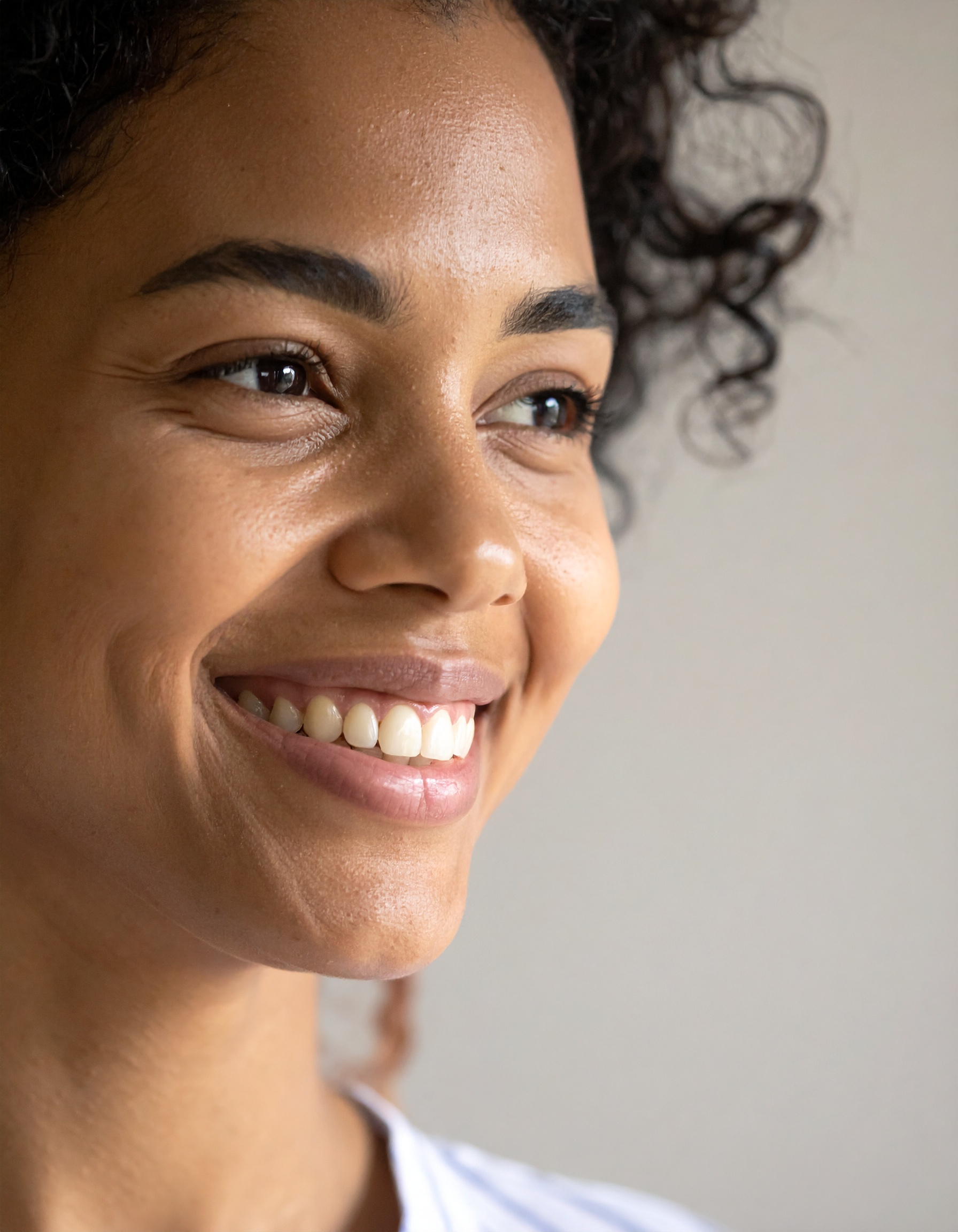 A woman with radiant skin and a joyful smile looks to the side