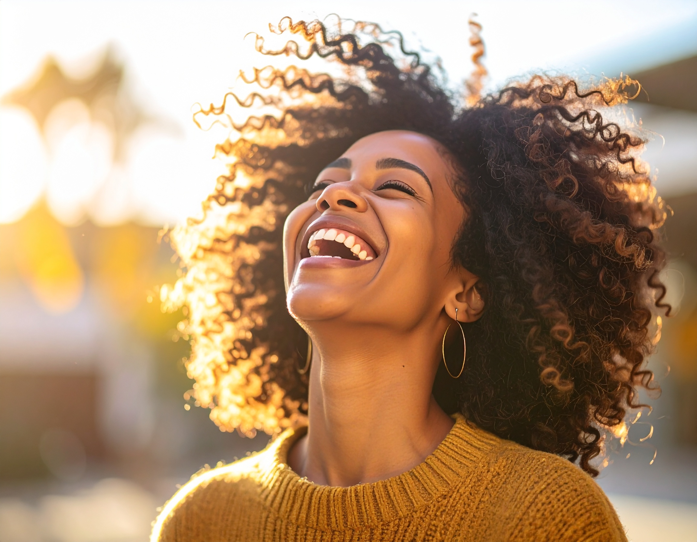 A woman with curly hair laughs joyfully in the golden sunlight