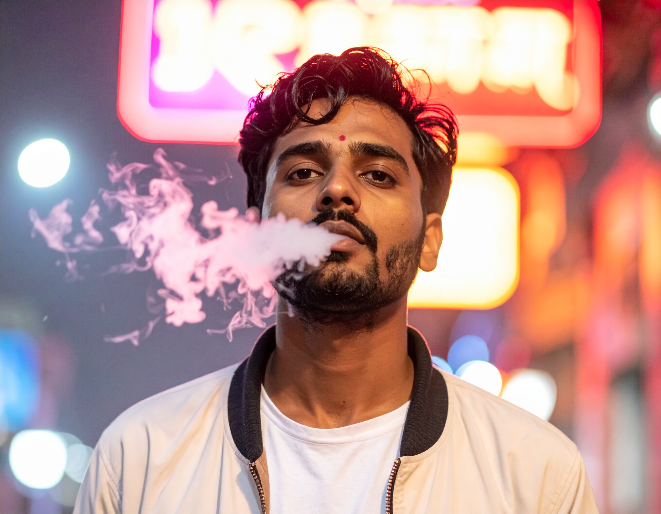 A stylish man emits vapor in front of neon city lights