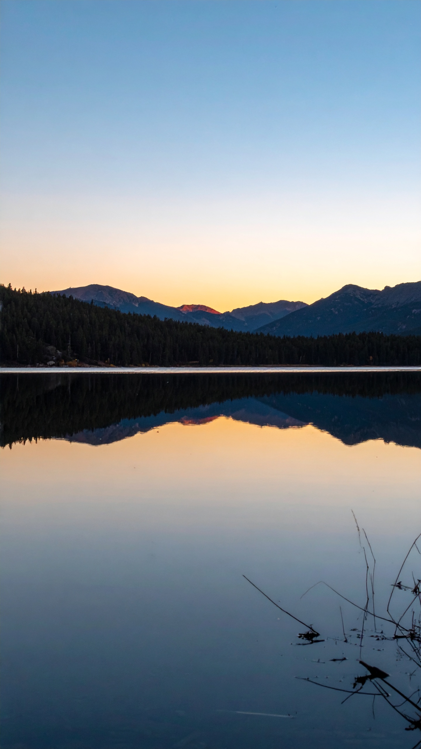 A serene lake reflects a stunning sunset with silhouetted mountains