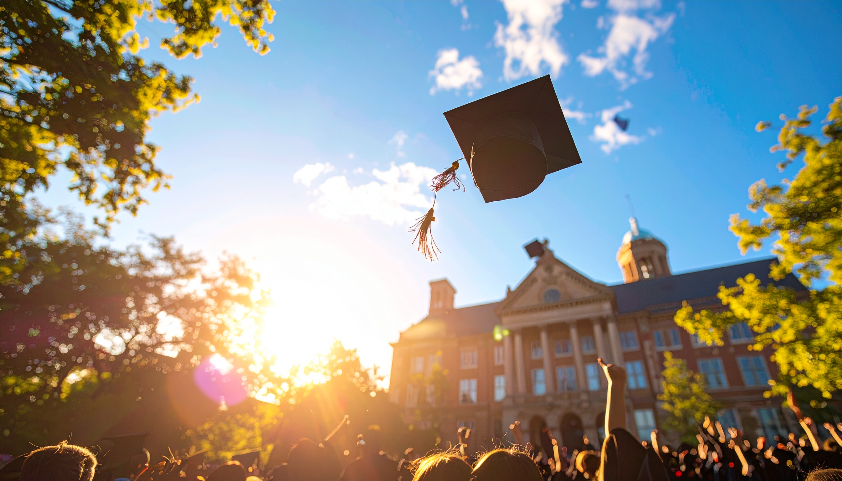 Graduates Celebrate Outdoors Throwing Caps Under Blue Sky