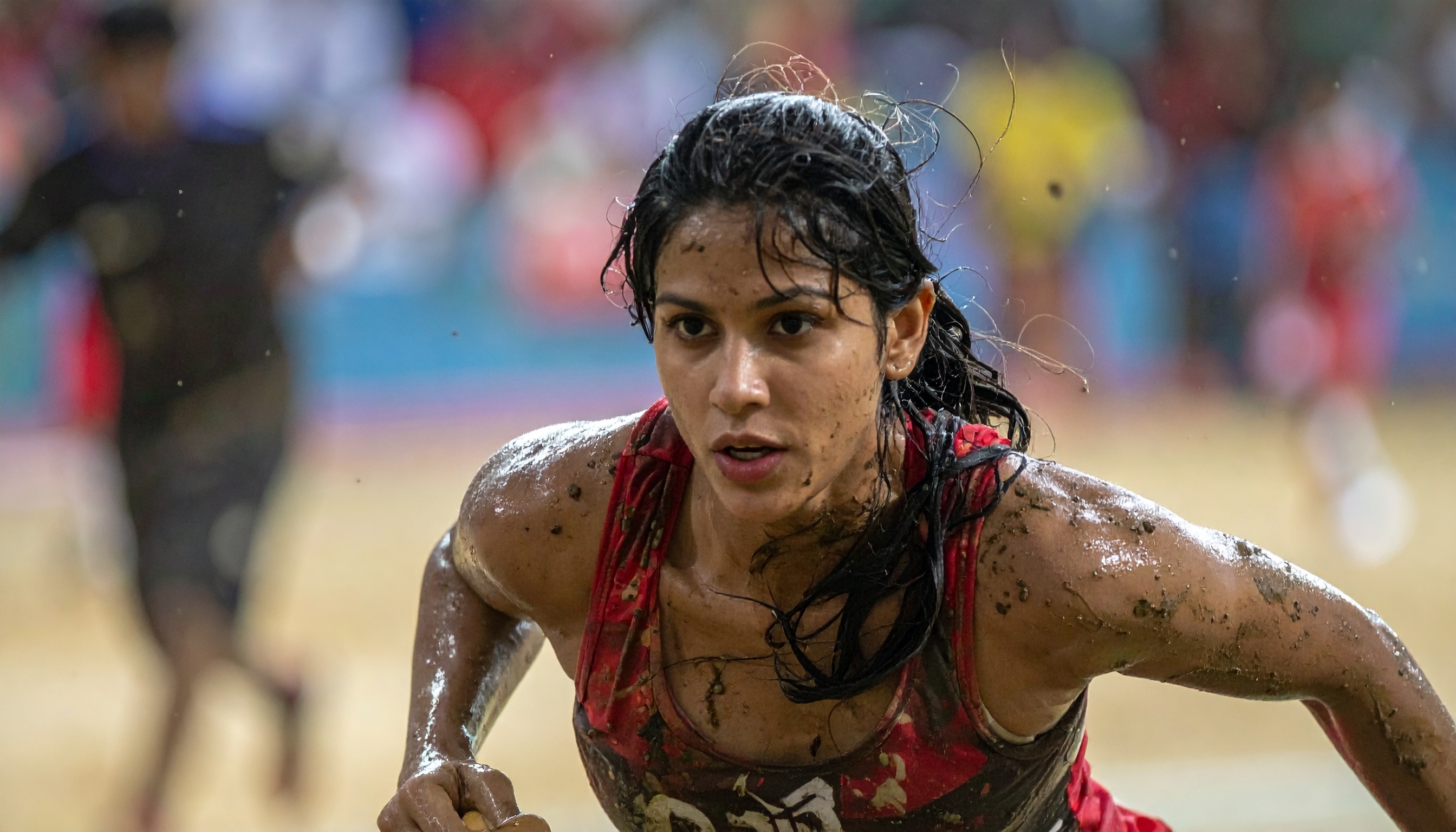 A determined athlete competes in a mud-filled challenge, showcasing intense focus and resilience