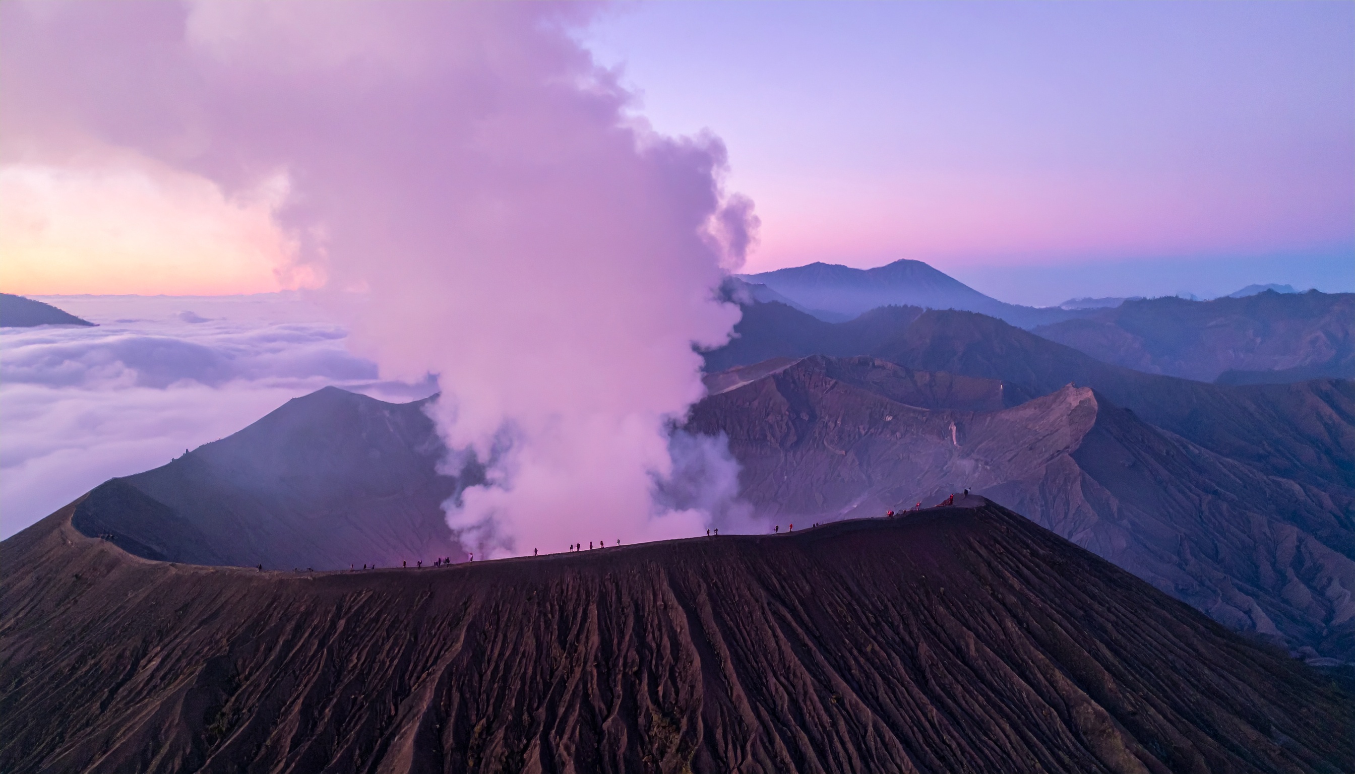 O vulcão Monte Bromo se ergue majestoso sob um céu tingido de rosa e lilás ao amanhecer. Este destino é popular para turistas que buscam aventuras e paisagens deslumbrantes na Indonésia. A imagem destaca o contraste entre a fumaça branca que emana da cratera e as sombras escuras do terreno vulcânico. Ideal para usar em campanhas de turismo e promoção de viagens exóticas, capturando a essência de uma experiência única. A beleza natural e a aura mística fazem deste local um ponto de atração imperdível.