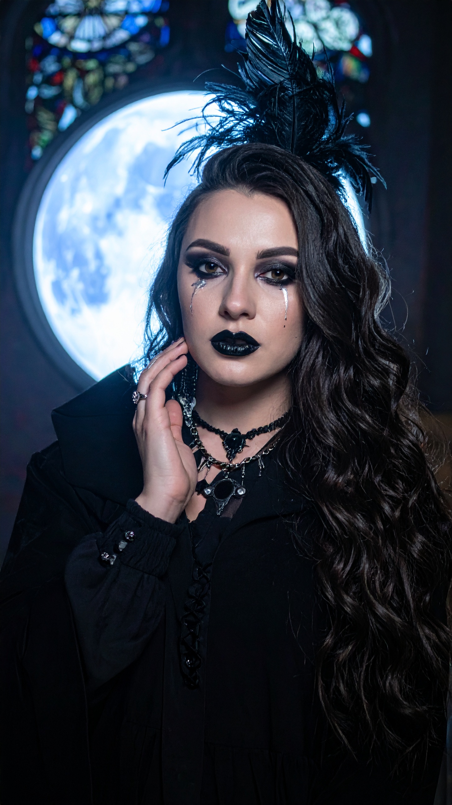 A mulher apresenta um visual gótico sofisticado com maquiagem dramática e acessórios elegantes. Este estilo é ideal para eventos temáticos ou sessões fotográficas inspiradas em moda alternativa. Detalhes como o batom preto e o colar de pedras criam um visual impactante e misterioso. É perfeito para festas de Halloween ou encontros sociais em ambientes mais obscuros. A combinação de elementos clássicos e modernos confere um charme único e expressivo.