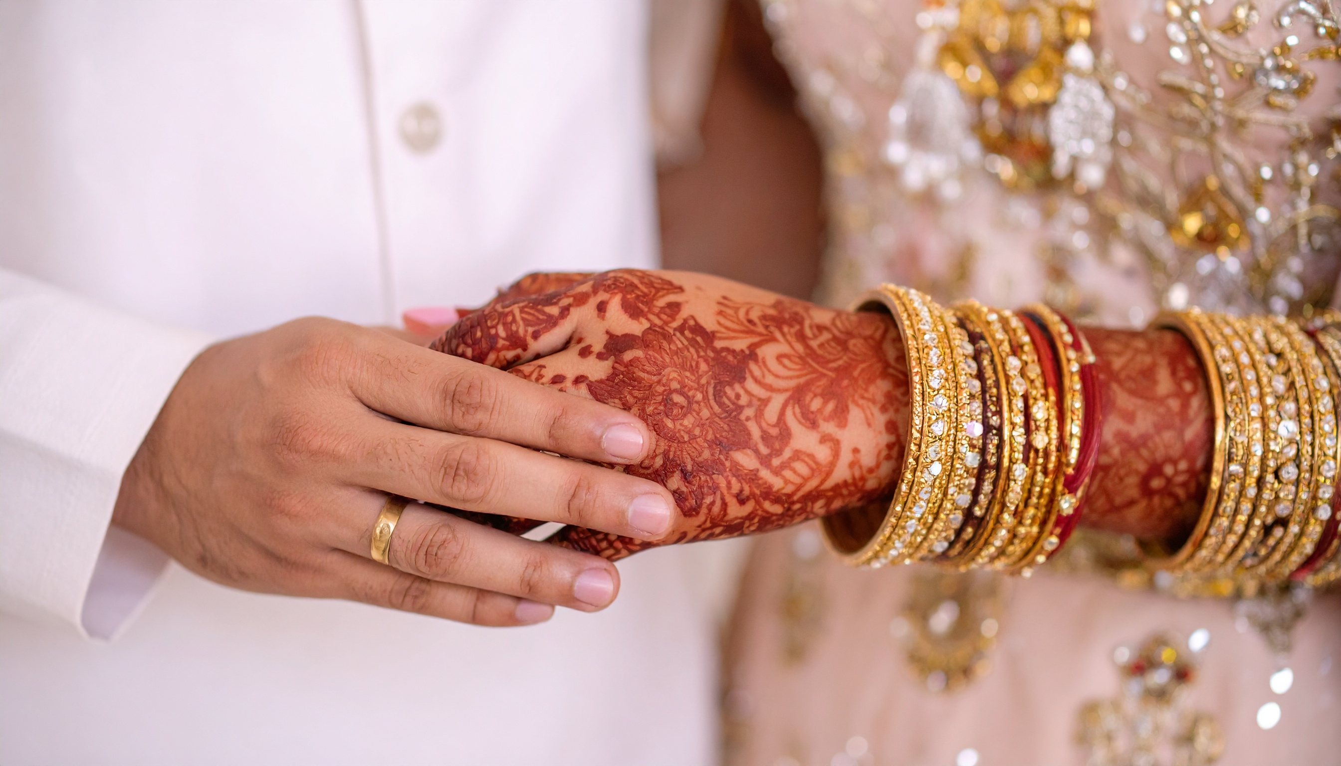 Intricate henna designs adorn a bride's hand, clasped by her partner's hand