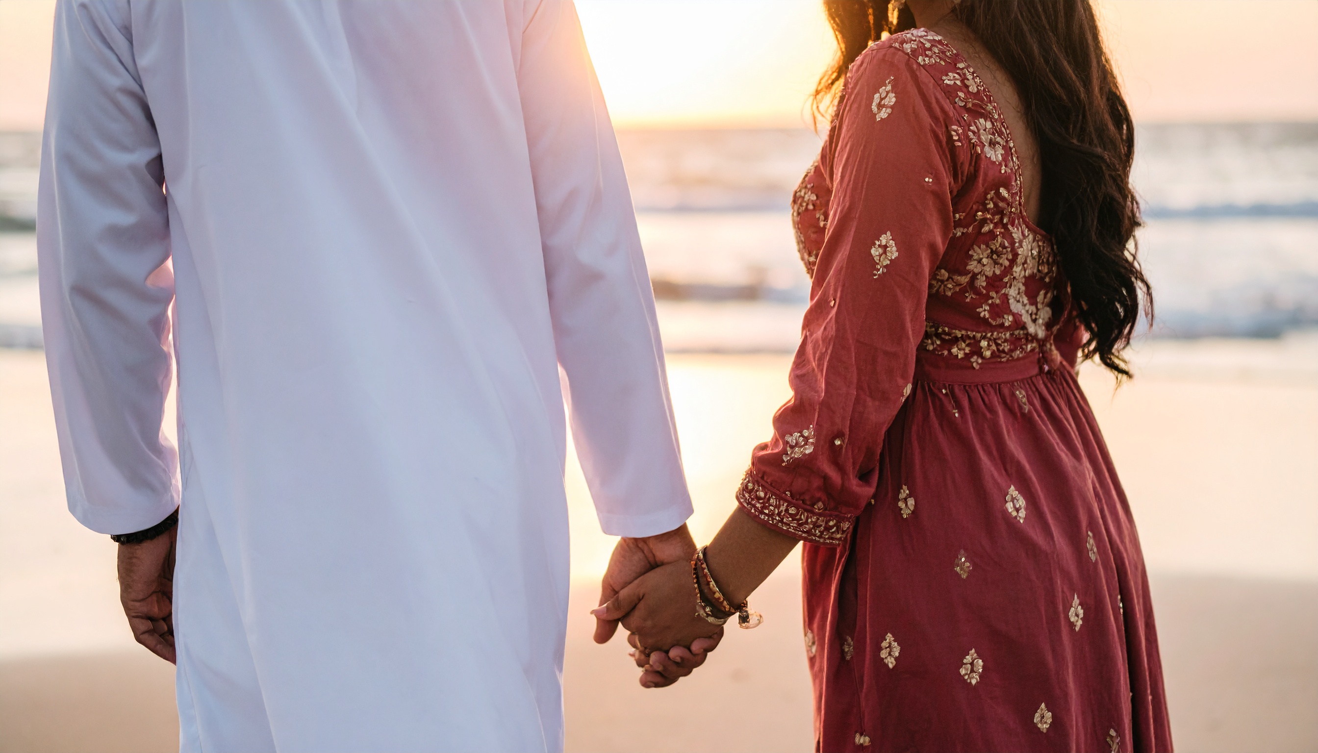 A couple holding hands at a serene beach during sunset