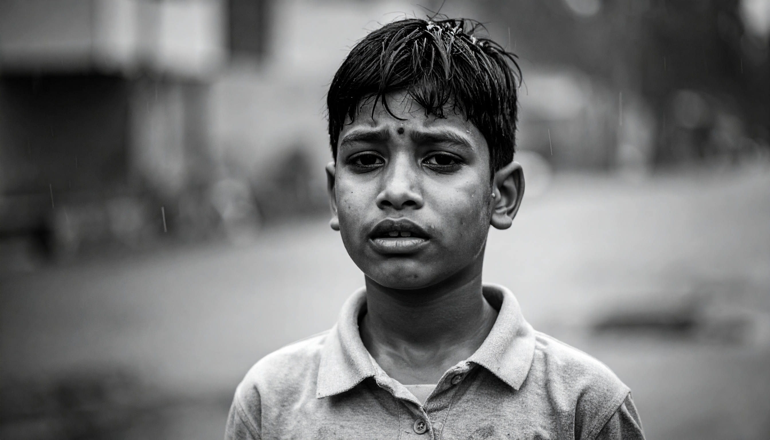 A young boy stands in the rain, looking directly into the camera