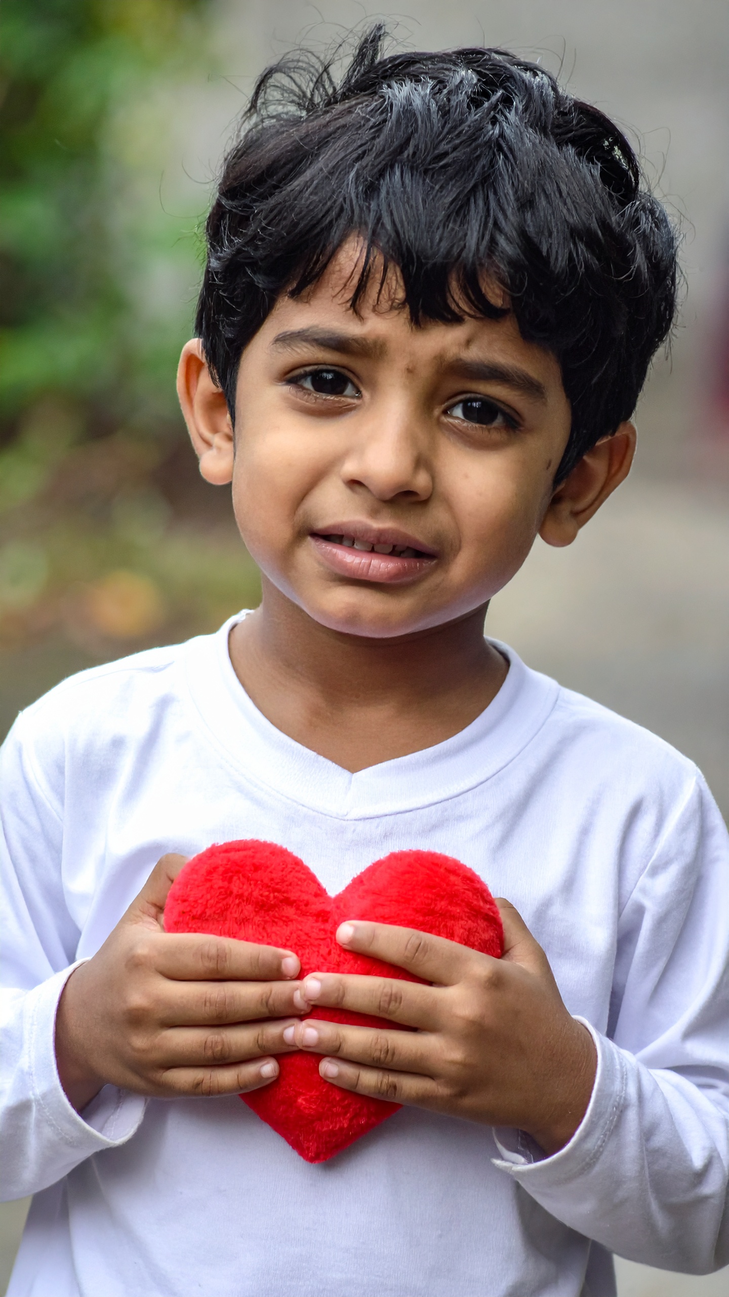 A child in a white shirt holds a plush red heart close, conveying warmth and sentiment
