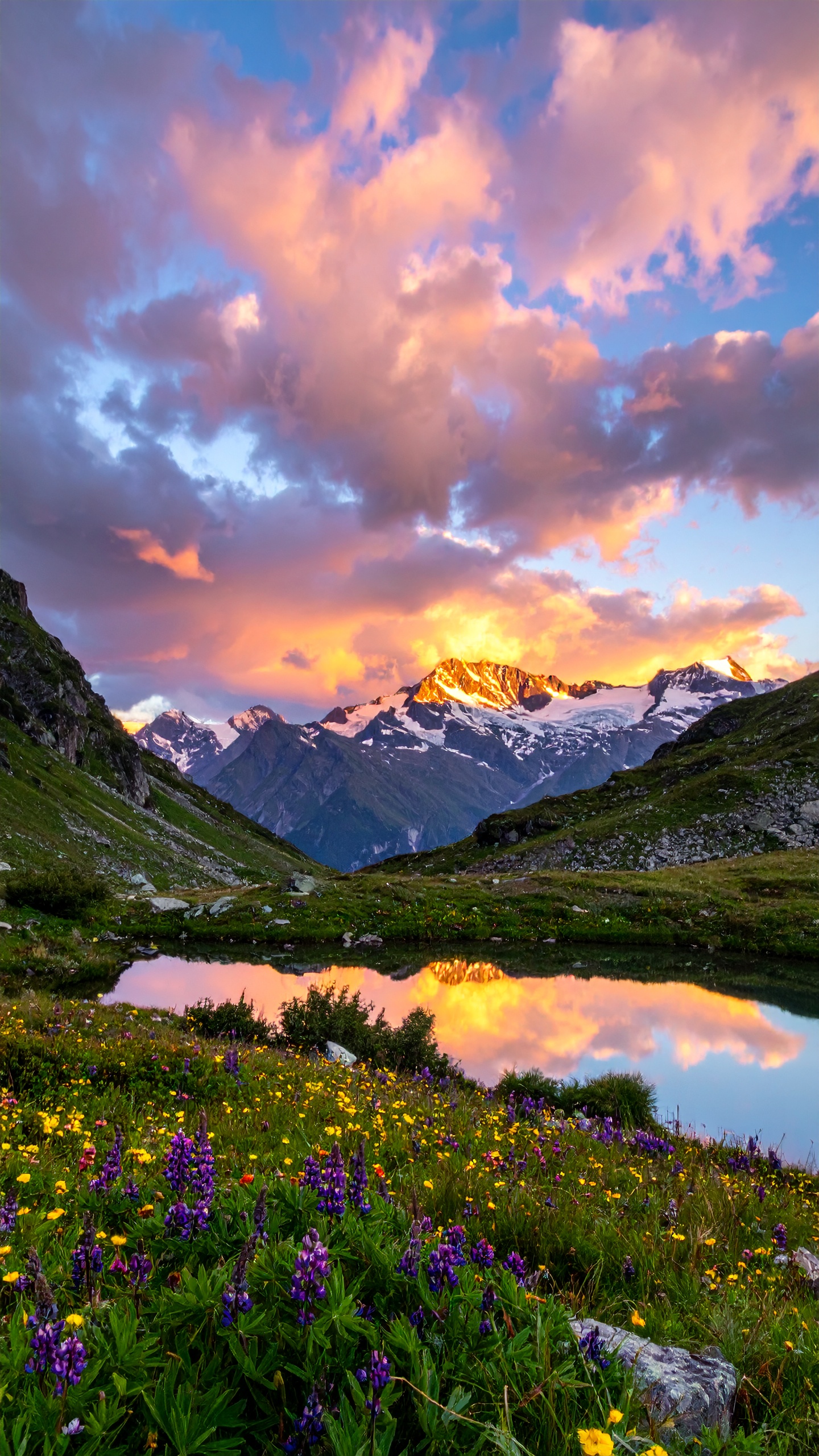 A stunning alpine landscape features snow-capped mountains glowing under a vibrant sunset sky