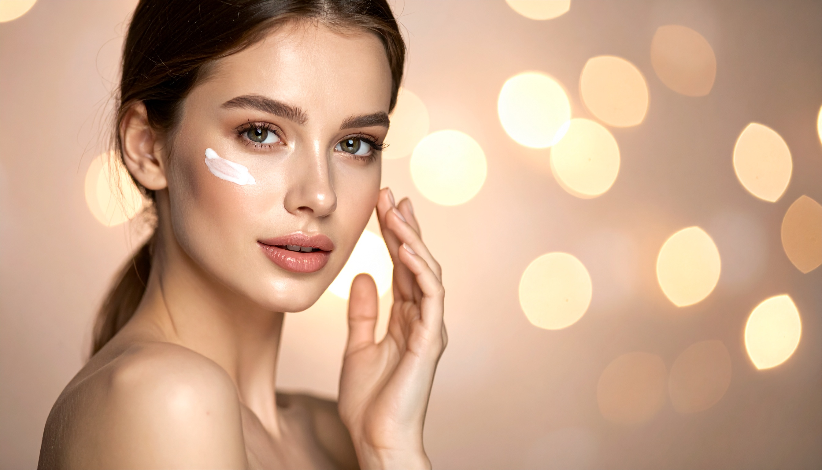 Retrato de uma jovem mulher com pele radiante aplicando creme facial, cercada por um fundo de luzes suaves e desfocadas, evocando uma atmosfera de beleza e cuidado pessoal.
