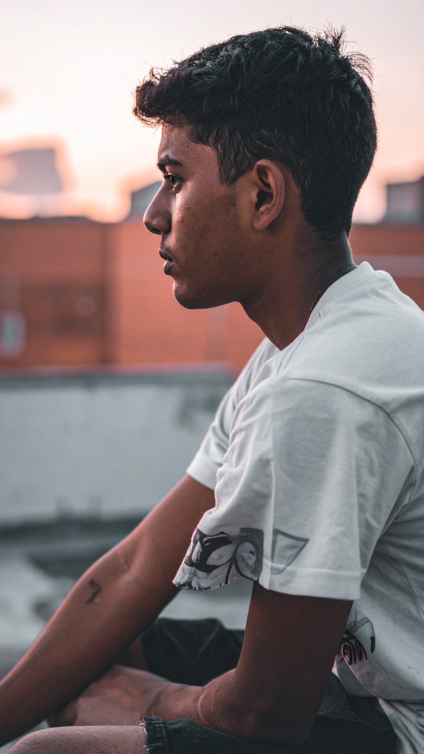 A young man sits contemplatively, silhouetted against a soft sunset sky