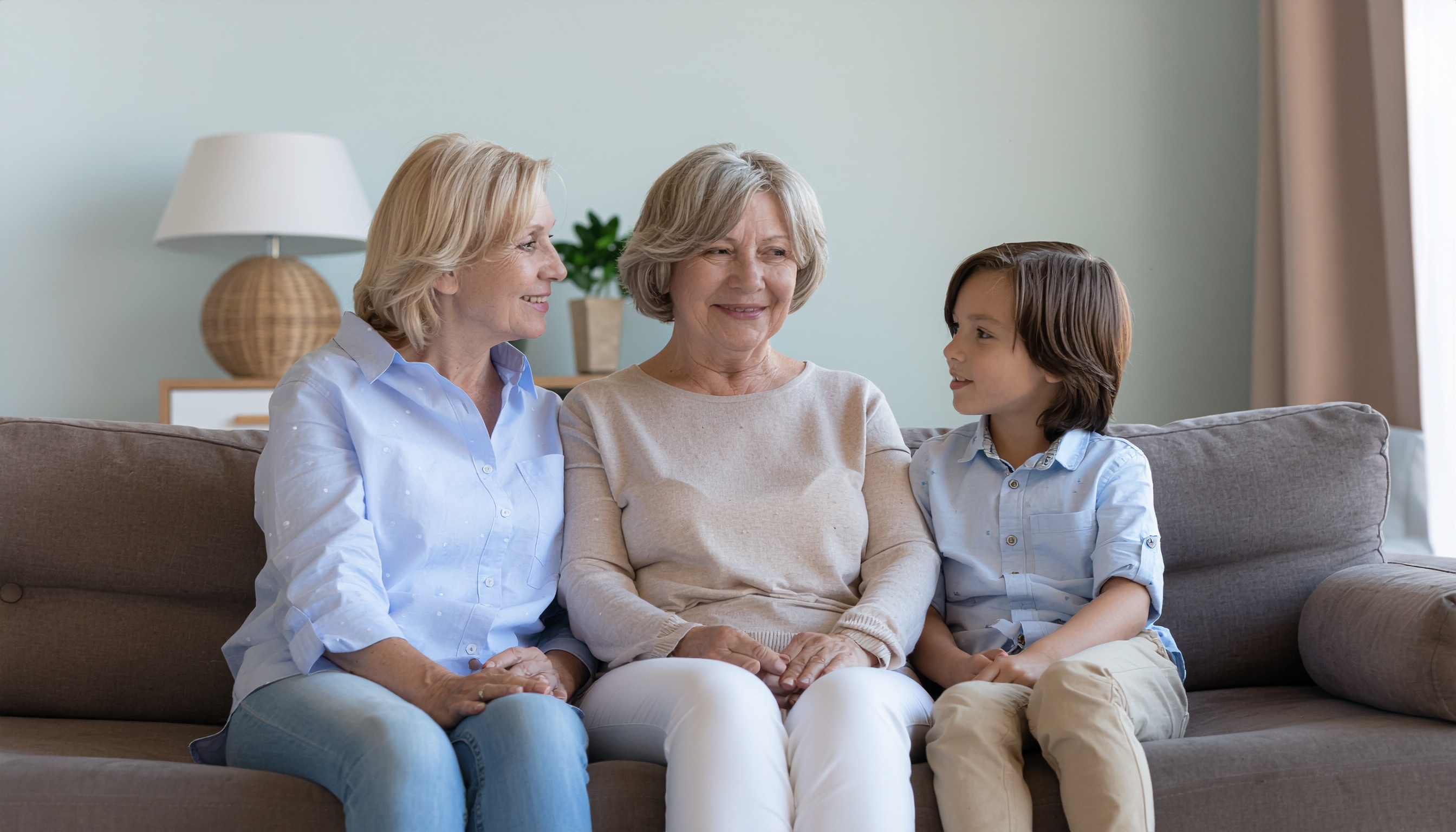 Three Generations on a Gray Sofa in a Bright Living Room