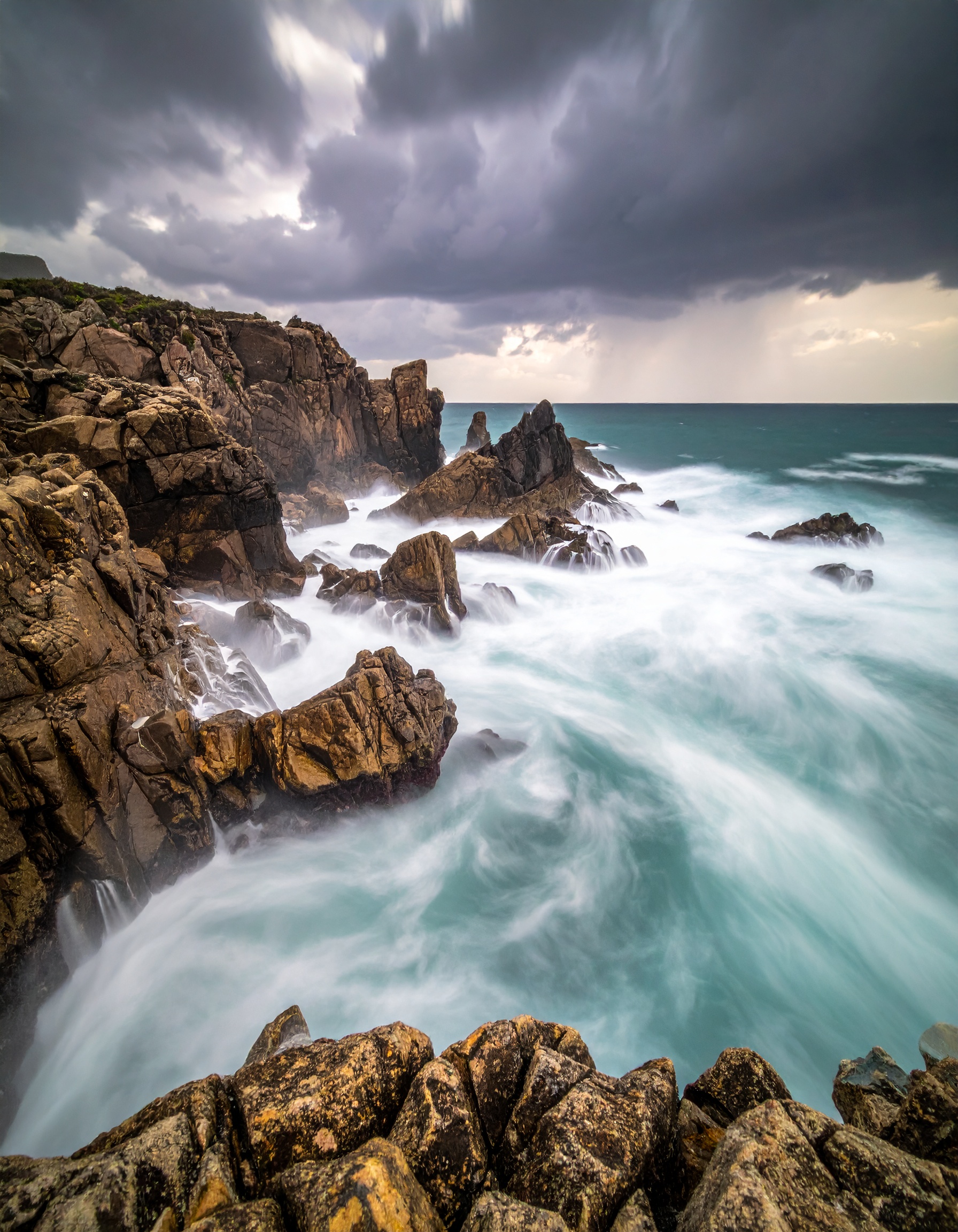 Dramatic coastal cliffs meet turbulent ocean waves under a stormy sky