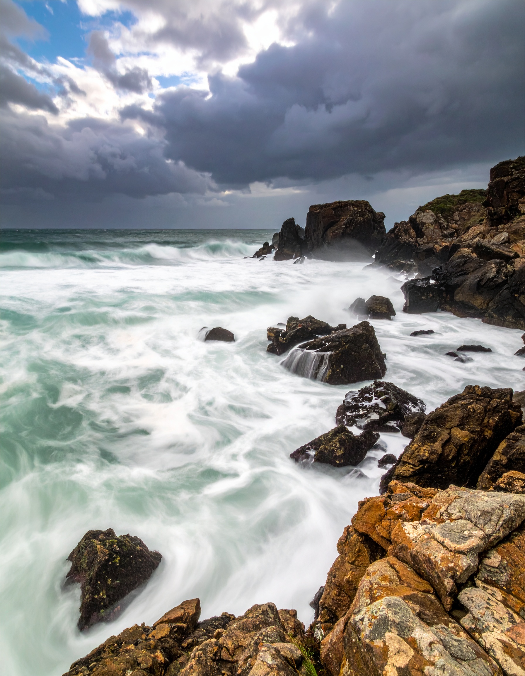 A dramatic coastal scene showcases powerful waves crashing against rugged rocks under a stormy sky
